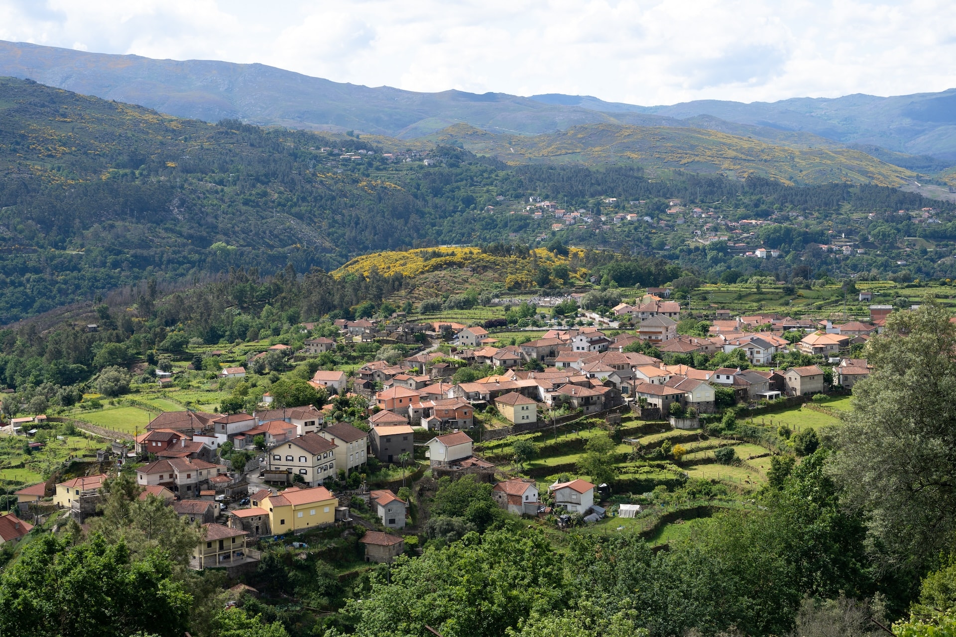 Village houses nestled in green terraces with forested mountains surrounding Soajo, Portugal.