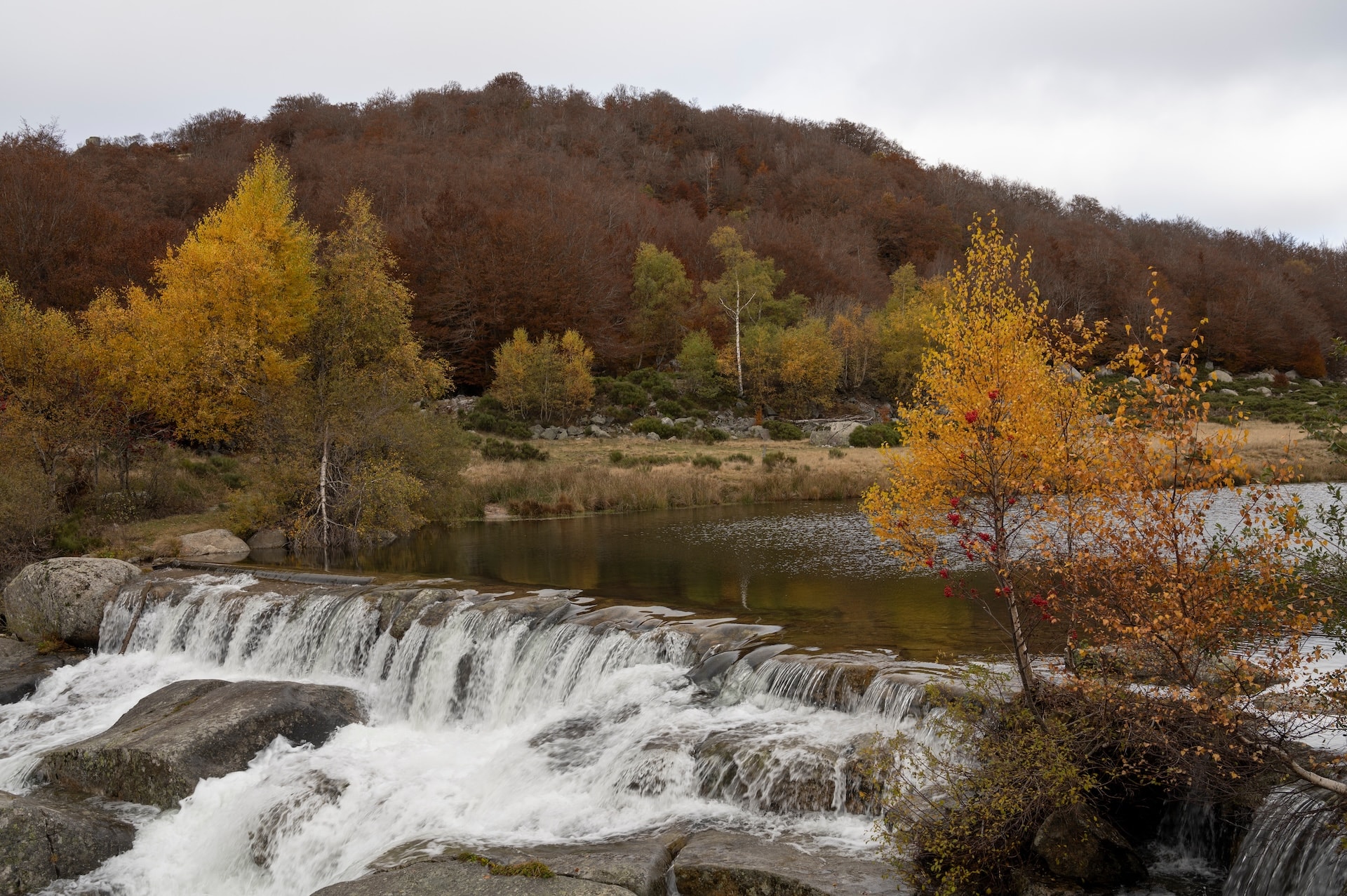 Waterfall cascading over rocks into a lake with autumn foliage in Lozère, Pont-de-Montvert.