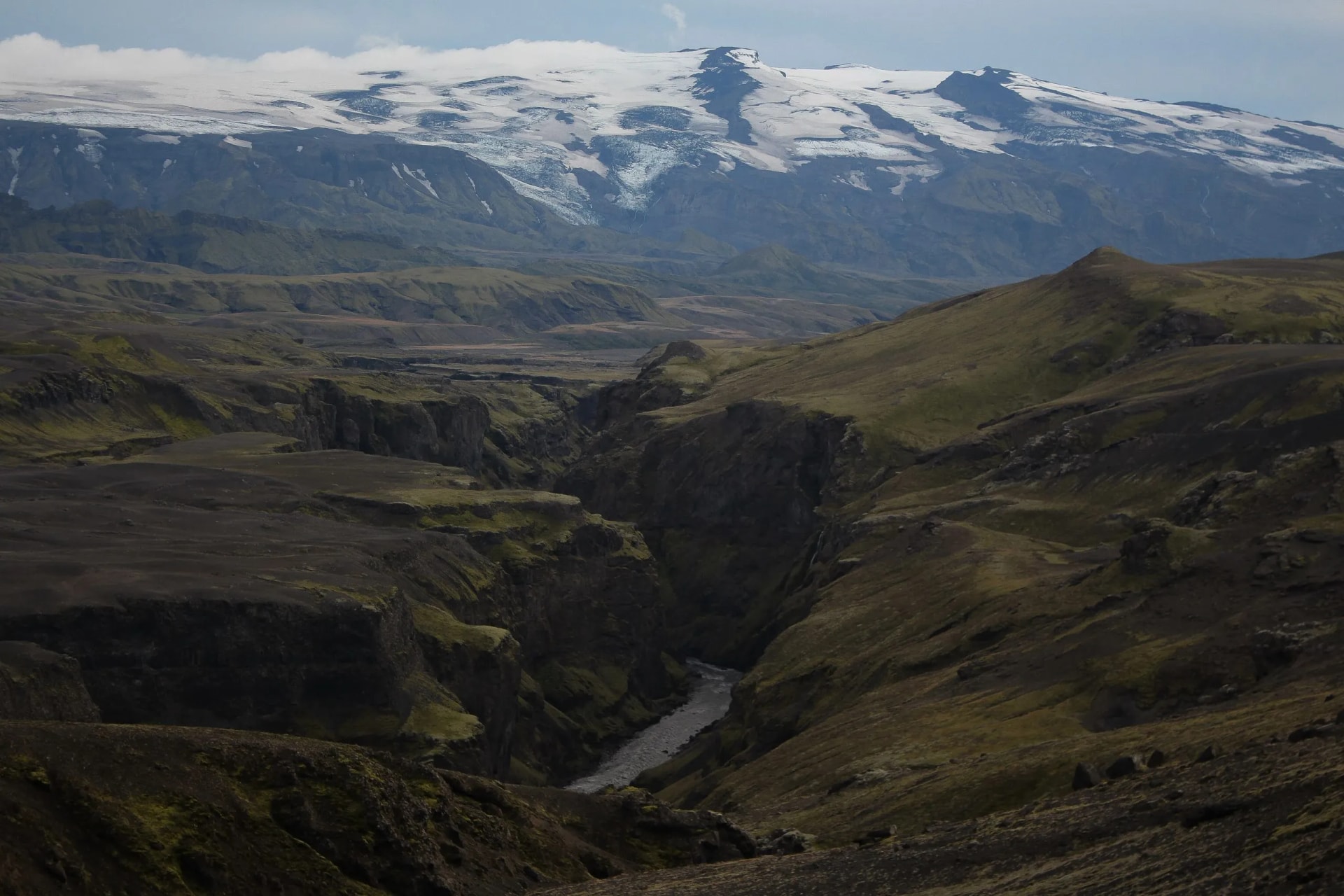 River flows through a deep canyon below the snow-capped Markarfljót and Eyjafjallajökull glacier.