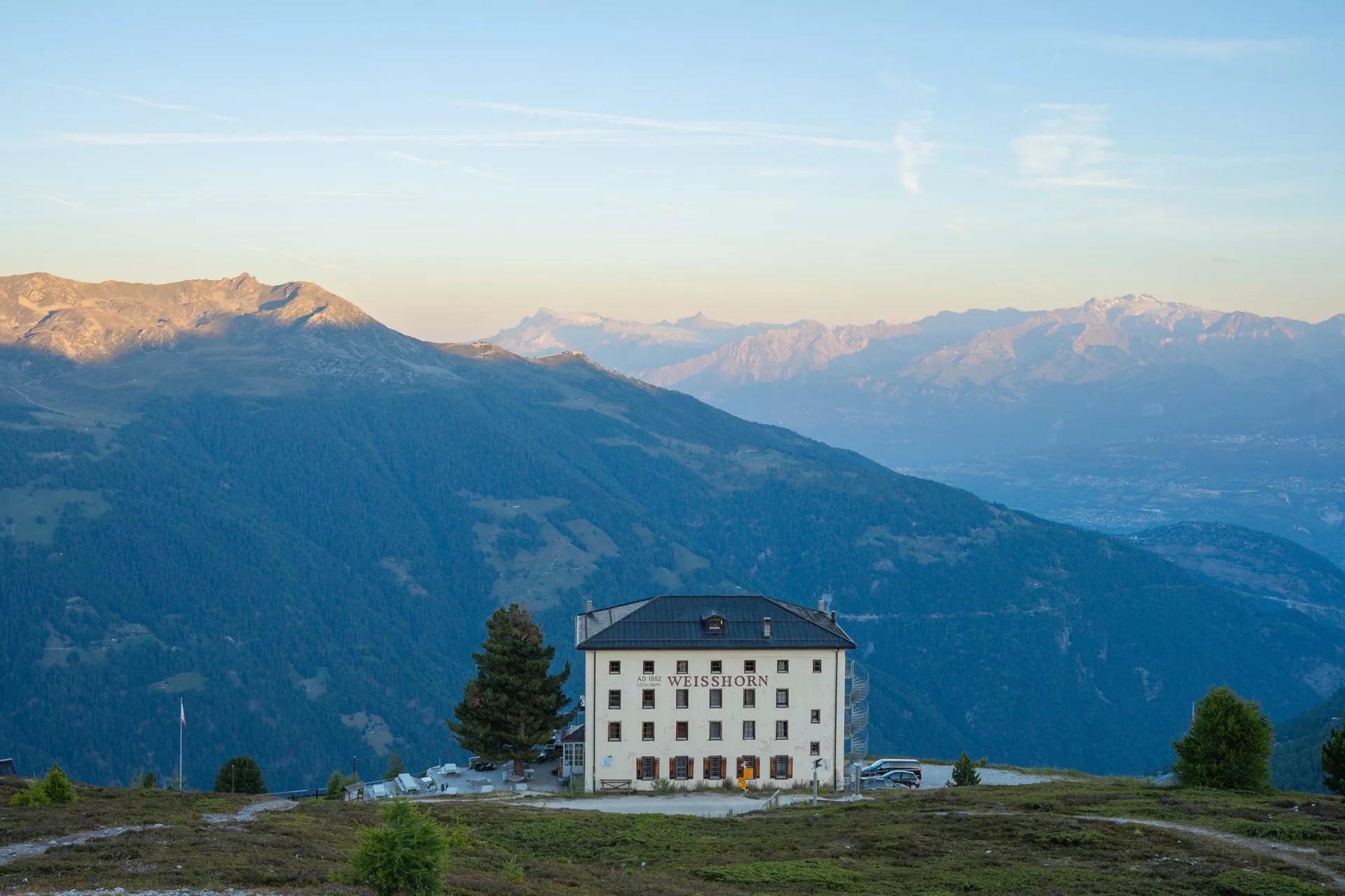 Hotel Weisshorn building on grassy mountain slope with layered blue mountains in background