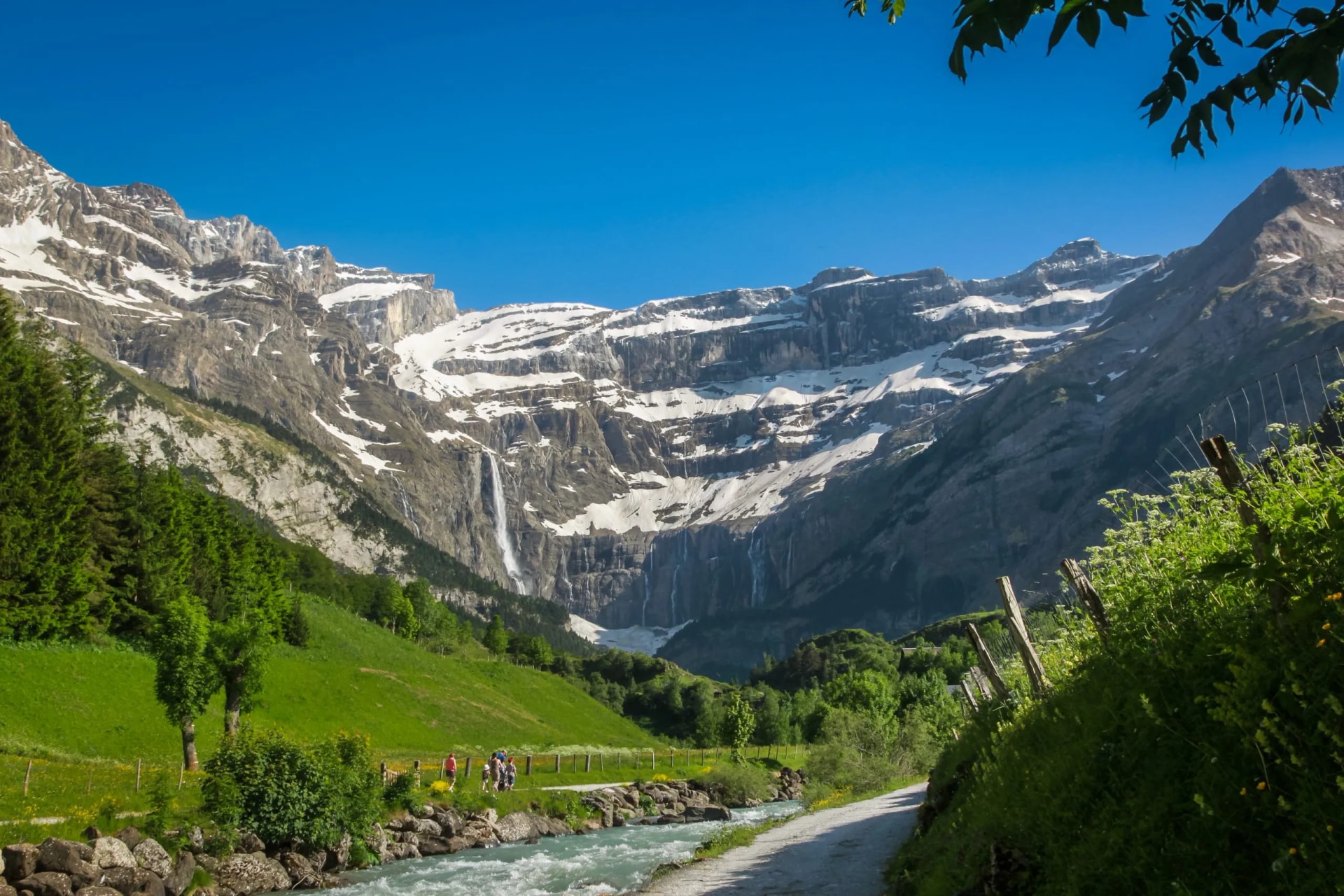 Cirque de Gavarnie waterfall cascading down snow-capped mountains above green valley and river.