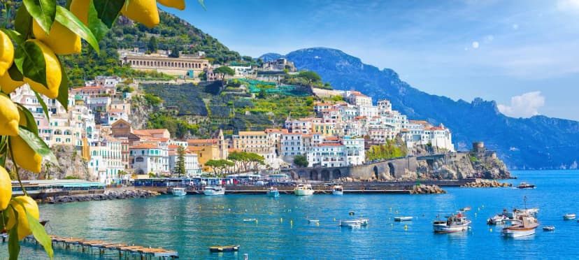 Lemons frame a panoramic view of colorful Amalfi town buildings on hills above the blue Mediterranean Sea.