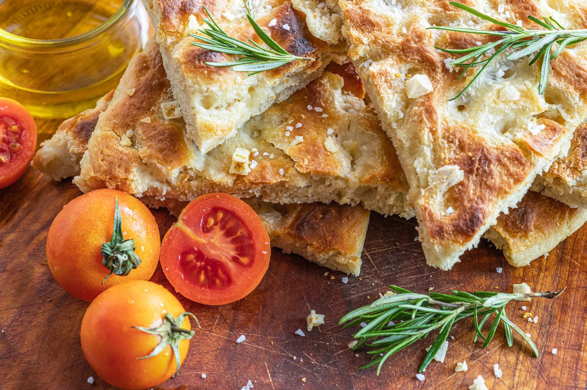 Slices of Ligurian focaccia with rosemary, tomatoes, and olive oil on a wooden board.