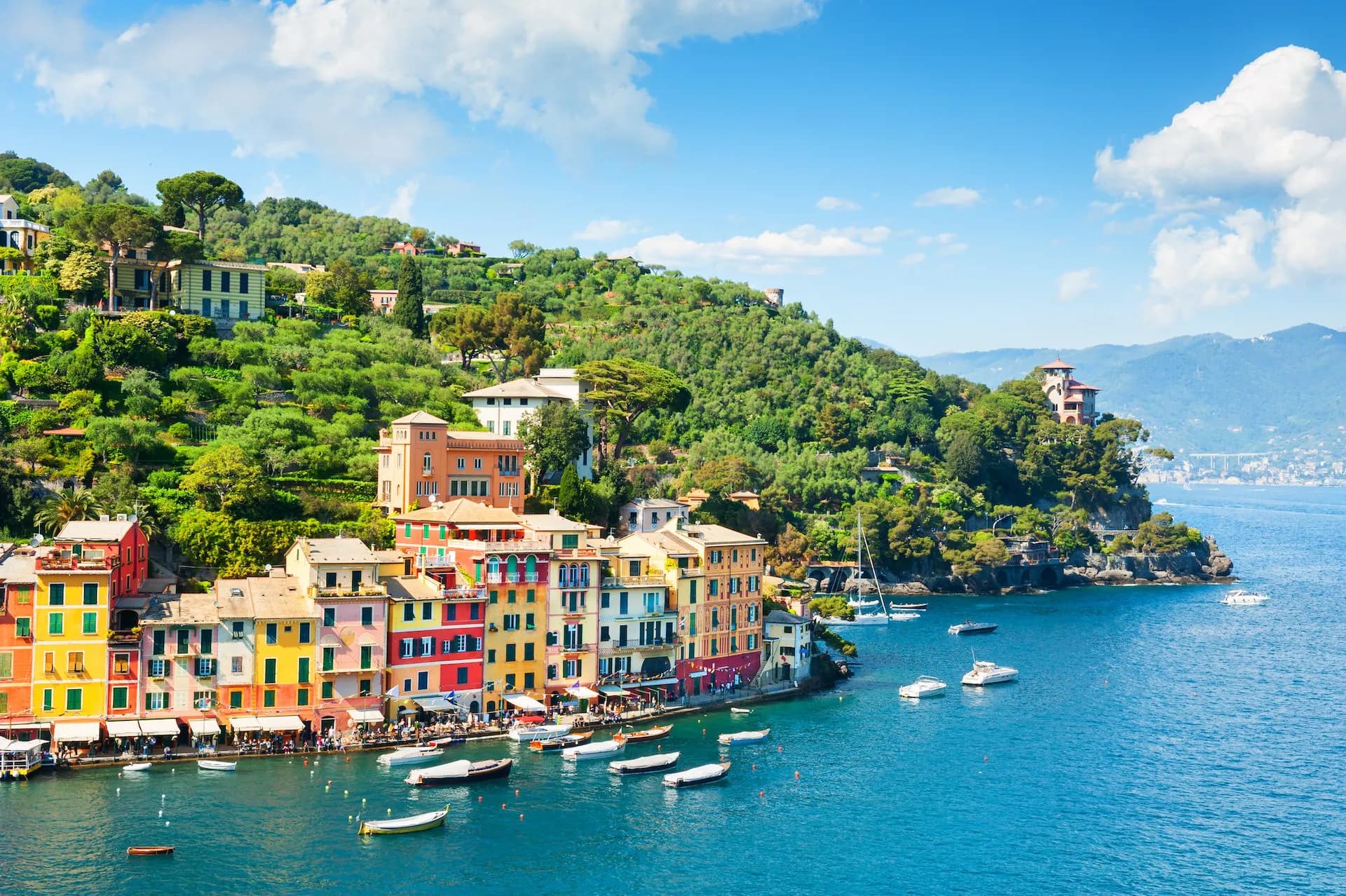 Colorful buildings line the harbor in Portofino with boats on the bright blue Mediterranean Sea.