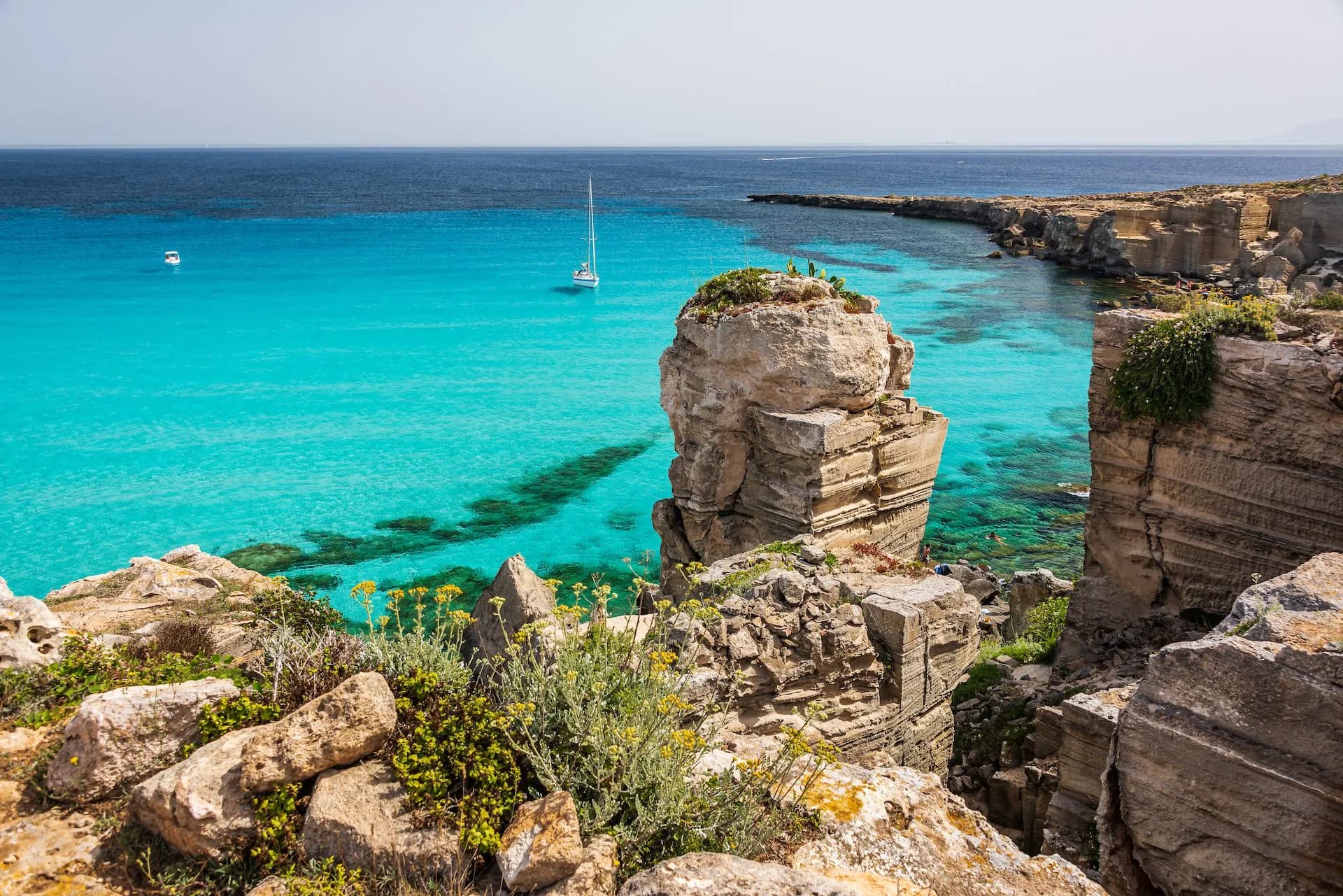 Sailboat on turquoise water near rocky cliffs at Cala Rossa, Favignana.