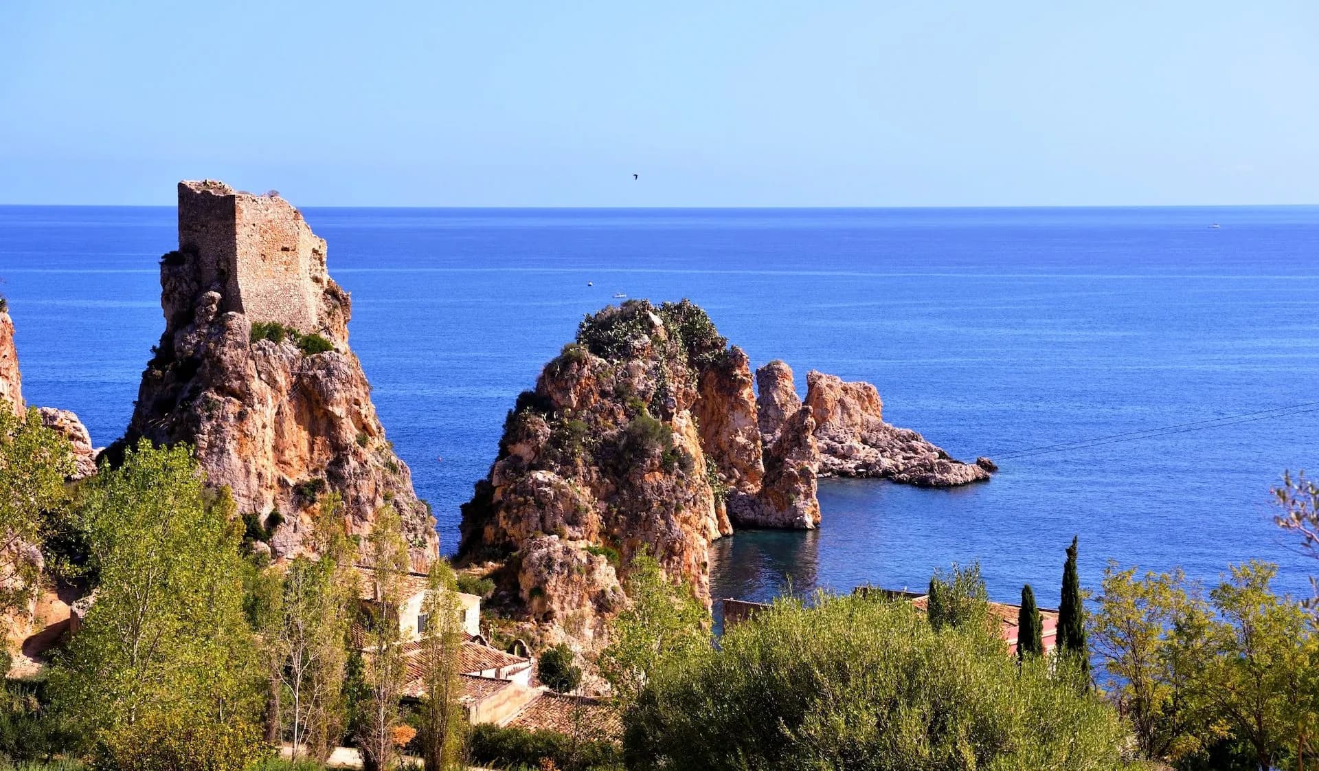 Ruins of Tonnara Tower on rocky outcrop above bright blue Mediterranean Sea at Scopello.
