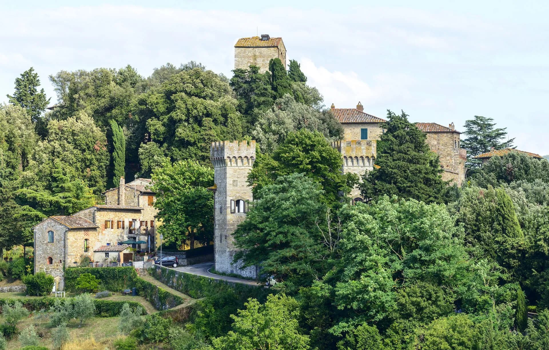 Stone towers and historic buildings nestled in lush green hillside foliage, likely Panzano.
