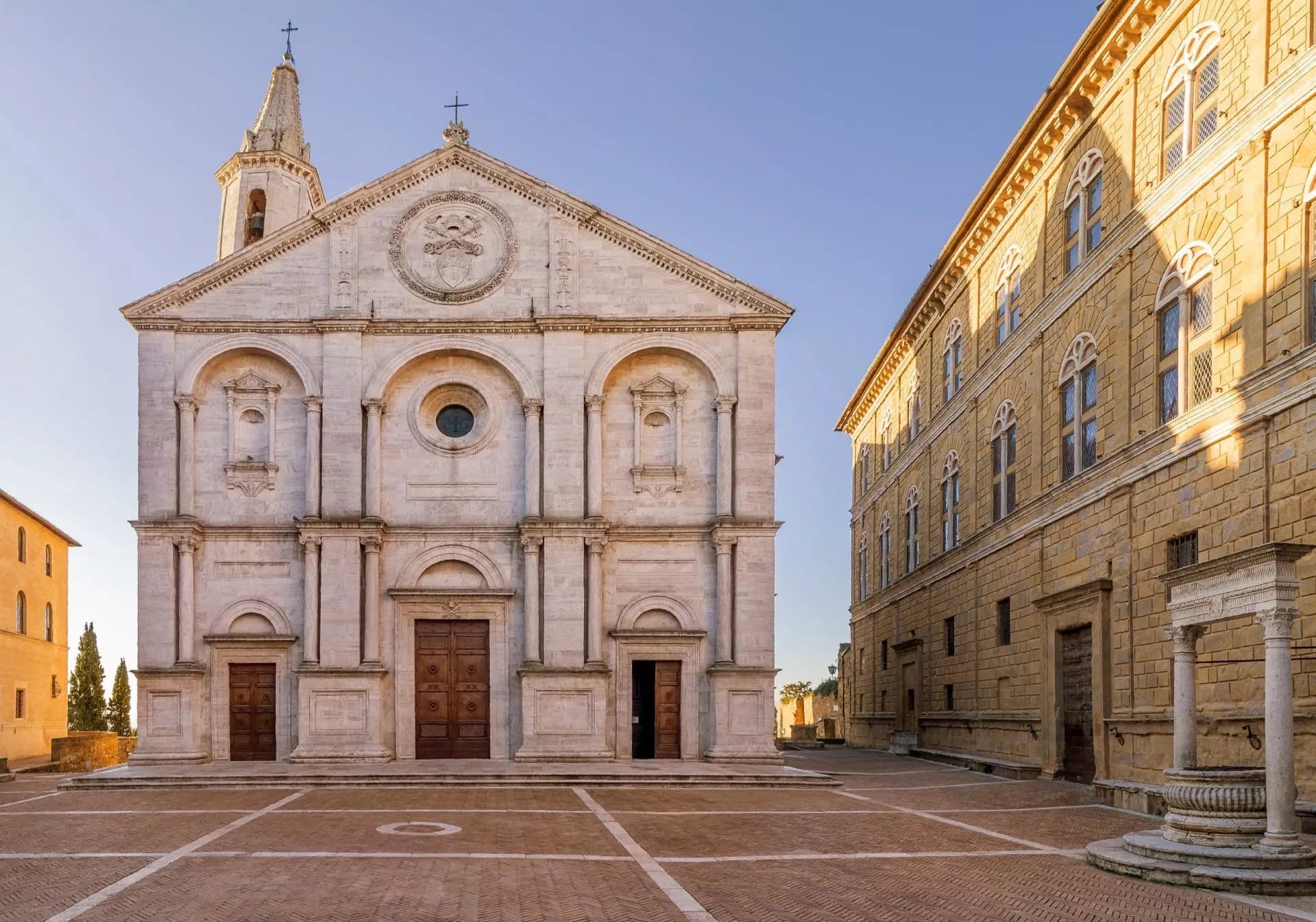 Pienza Cathedral facade in a historic square with a Renaissance palace on a sunny day.