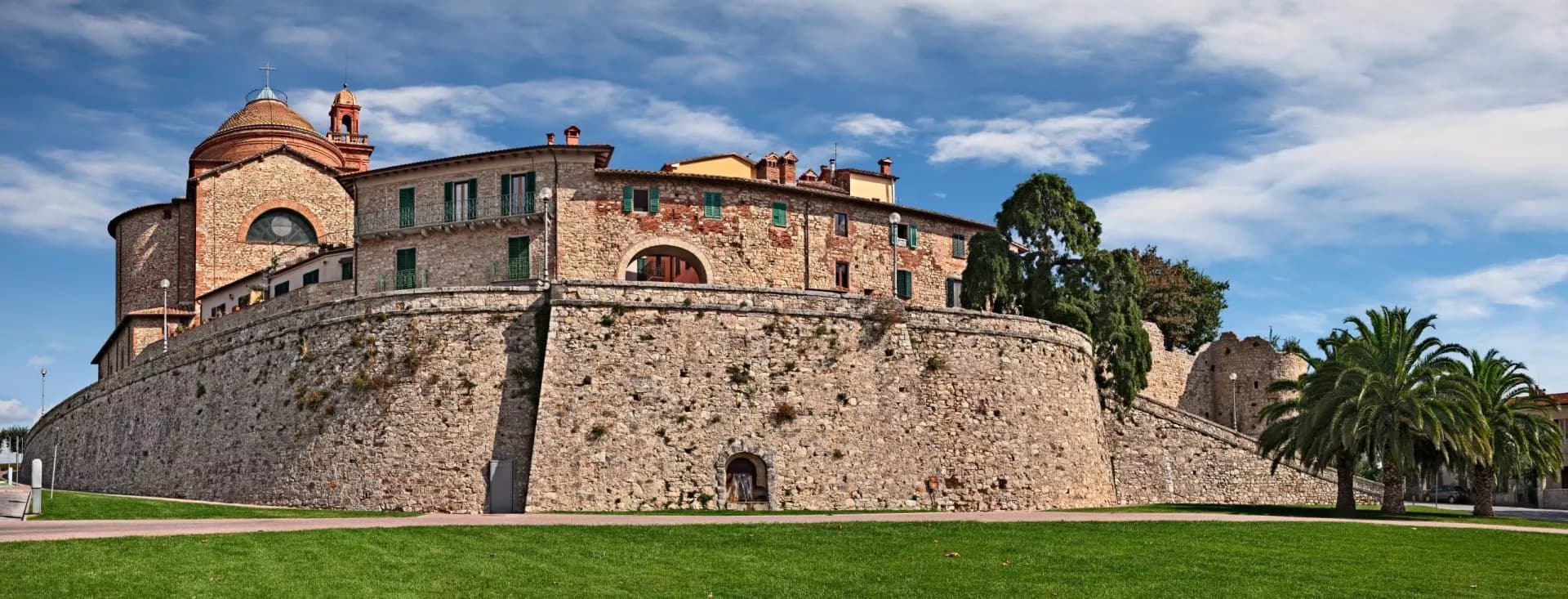 Historic stone fortress wall with buildings and dome church above, Castiglione del Lago.