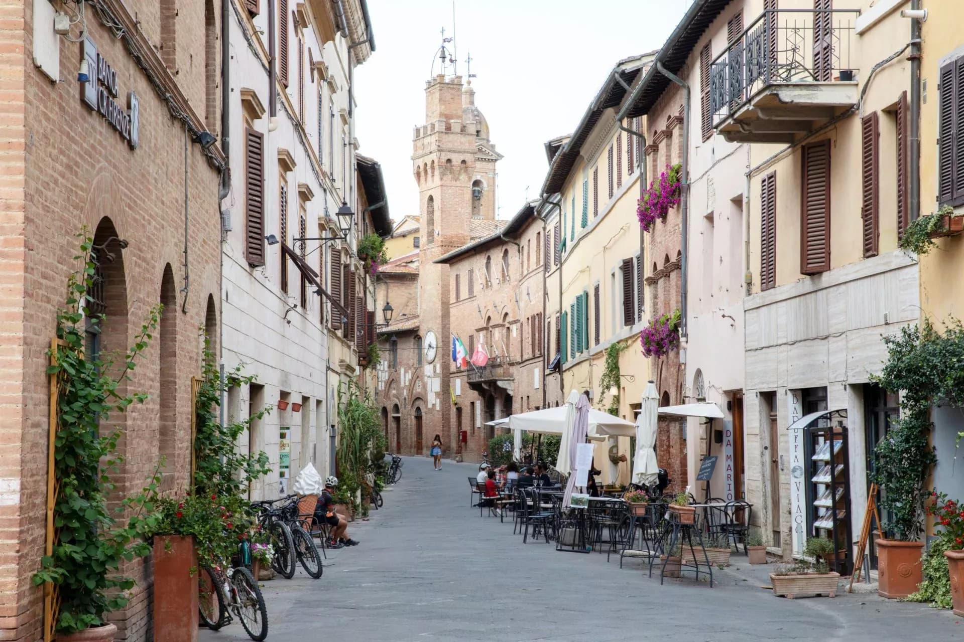 Narrow street in Buonconvento with historic buildings and outdoor cafe seating leading to a tower.