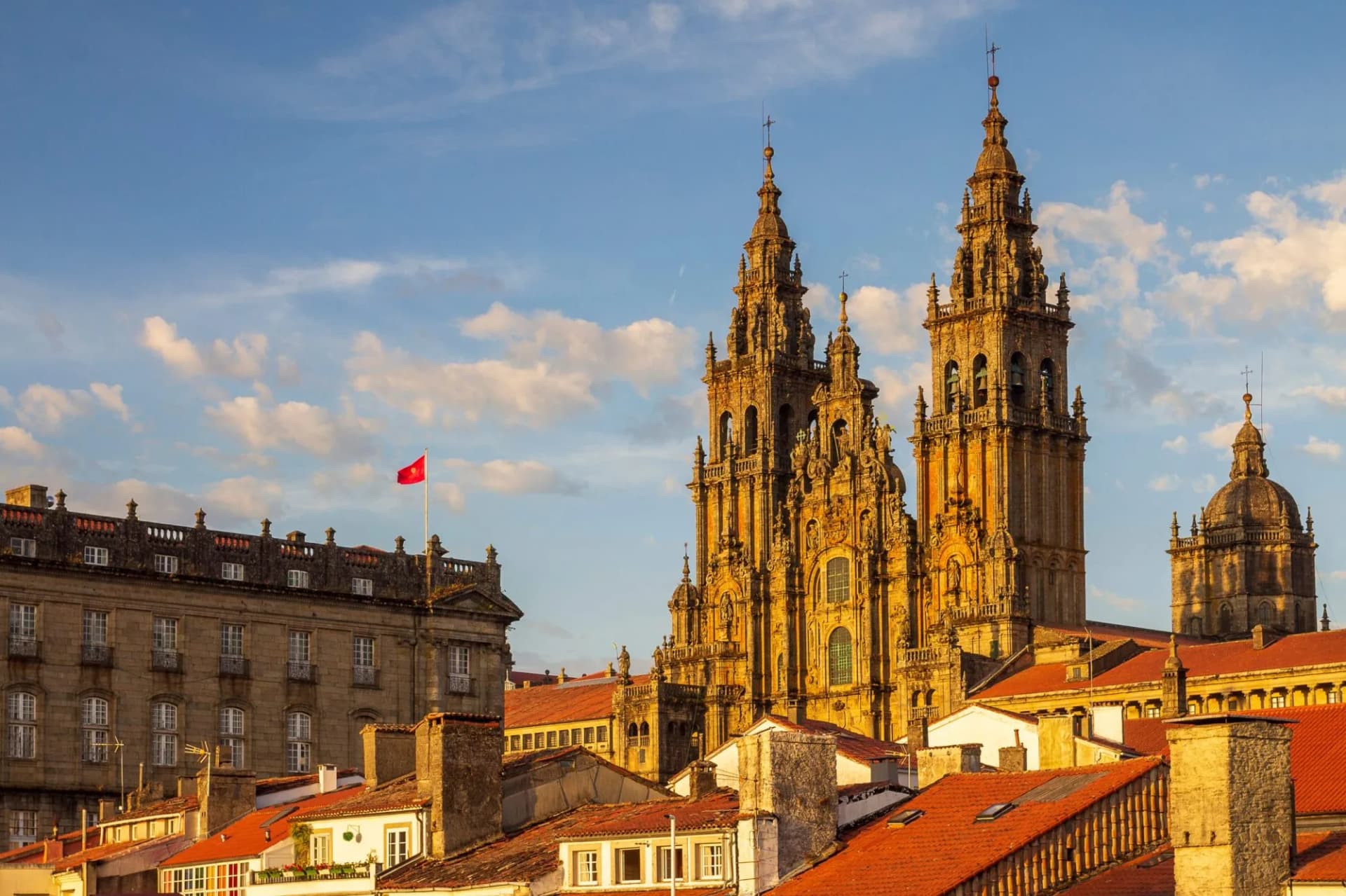 Santiago de Compostela Cathedral towers above terracotta rooftops under a blue, cloudy sky.