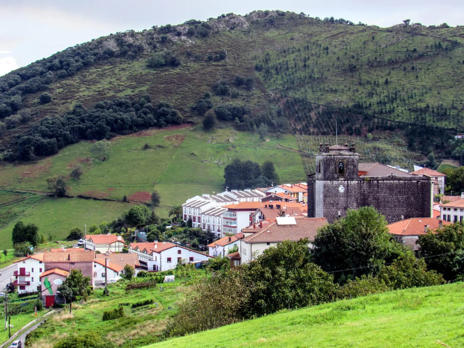 Cityscape of the small town of Markina nestled against a steep, green, tree-covered hillside.