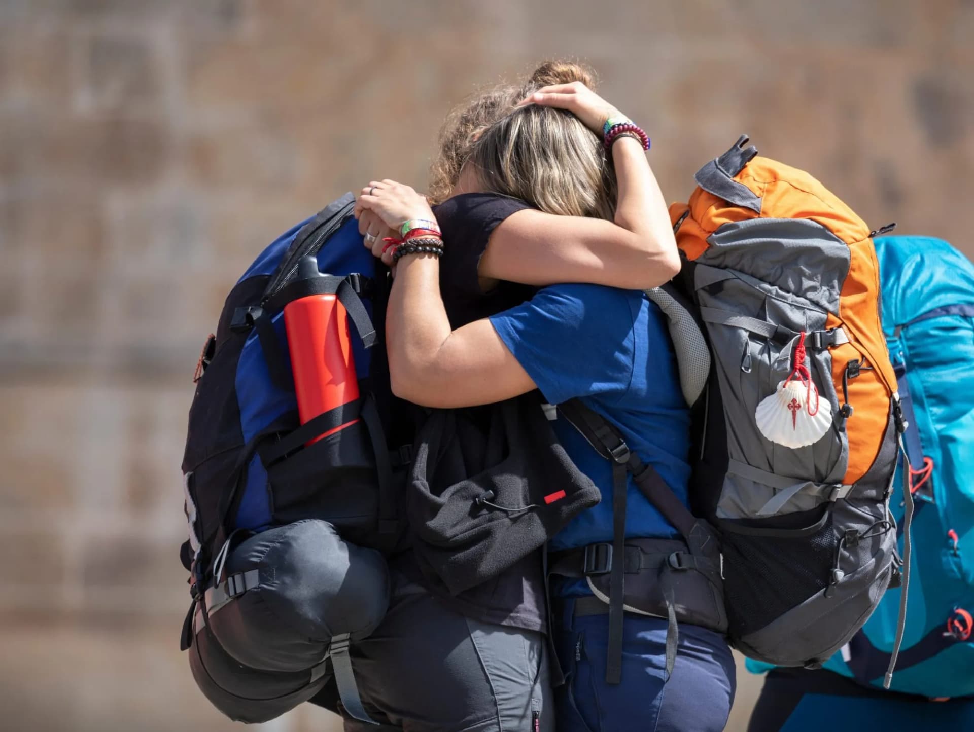 Pilgrims hugging with backpacks, one featuring a scallop shell, at Plaza del Obradoiro.