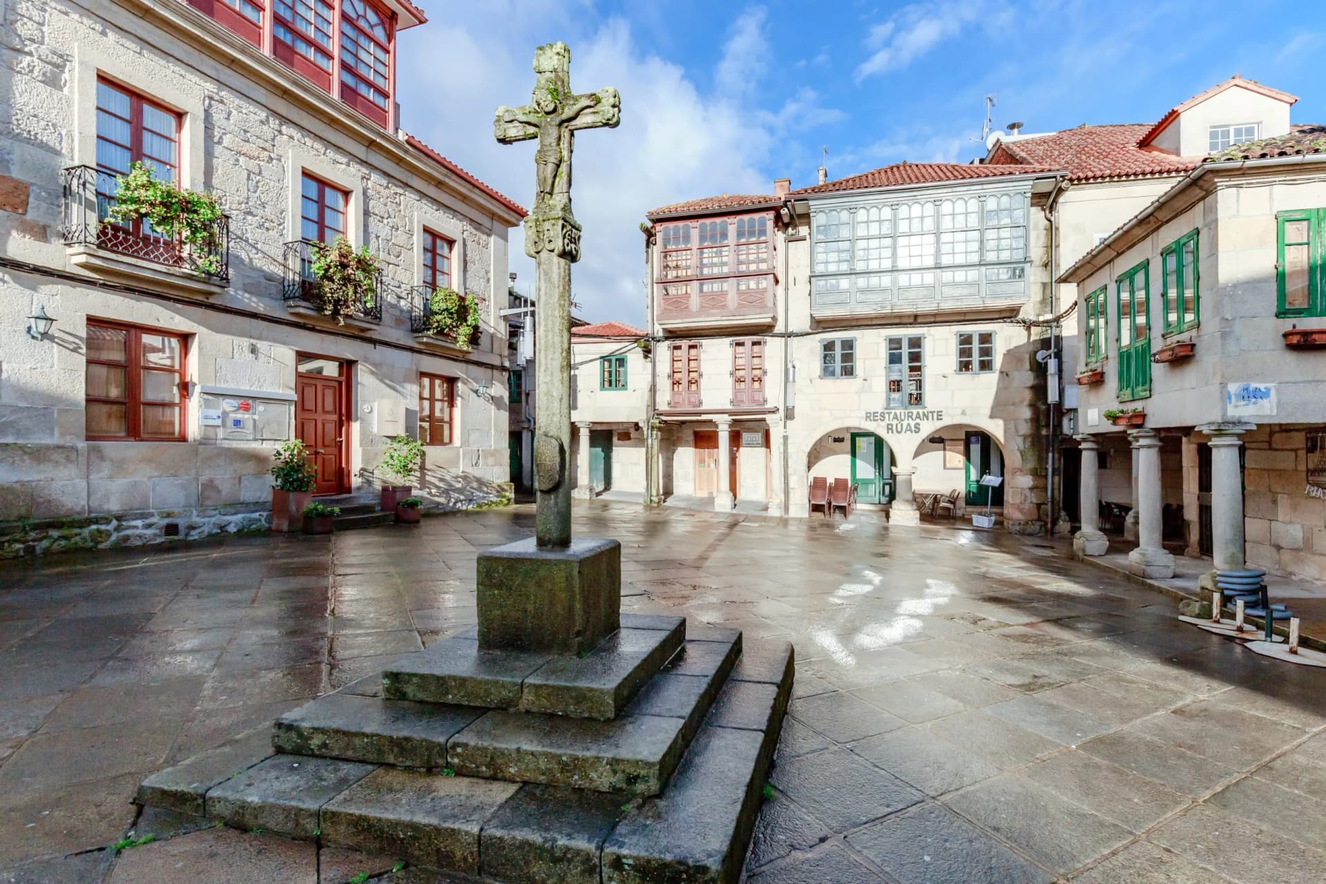 Stone calvary cross in a wet stone plaza surrounded by historic buildings in Pontevedra.