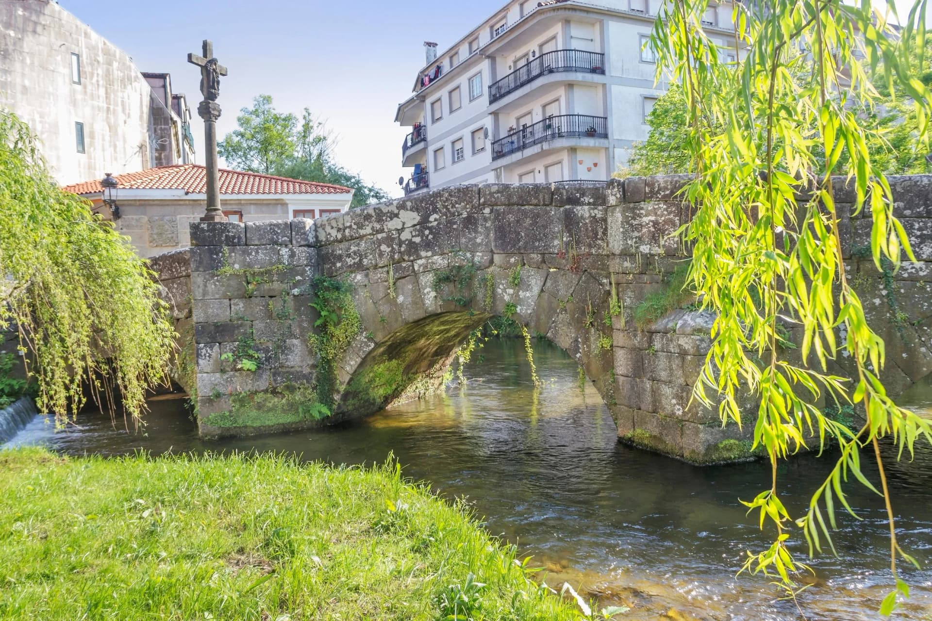 Stone Roman bridge over a stream with a wayside cross in Caldas de Reis.