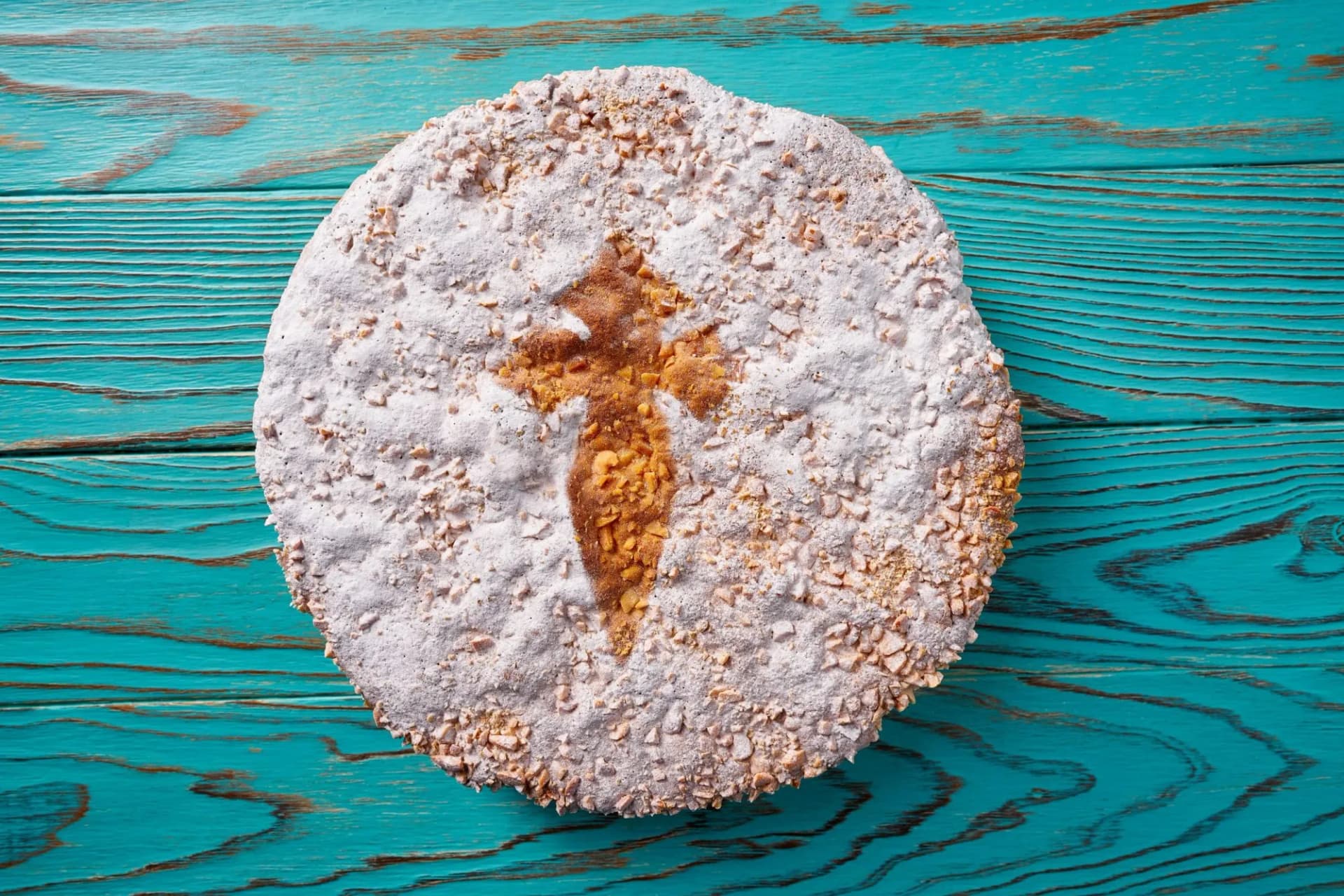 Tarta de Santiago almond cake with powdered sugar cross on bright turquoise wood background