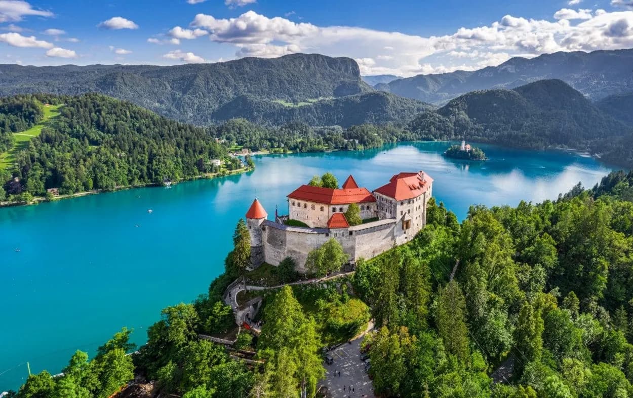 Lake Bled Castle on cliff above turquoise lake with island church and forested mountains.