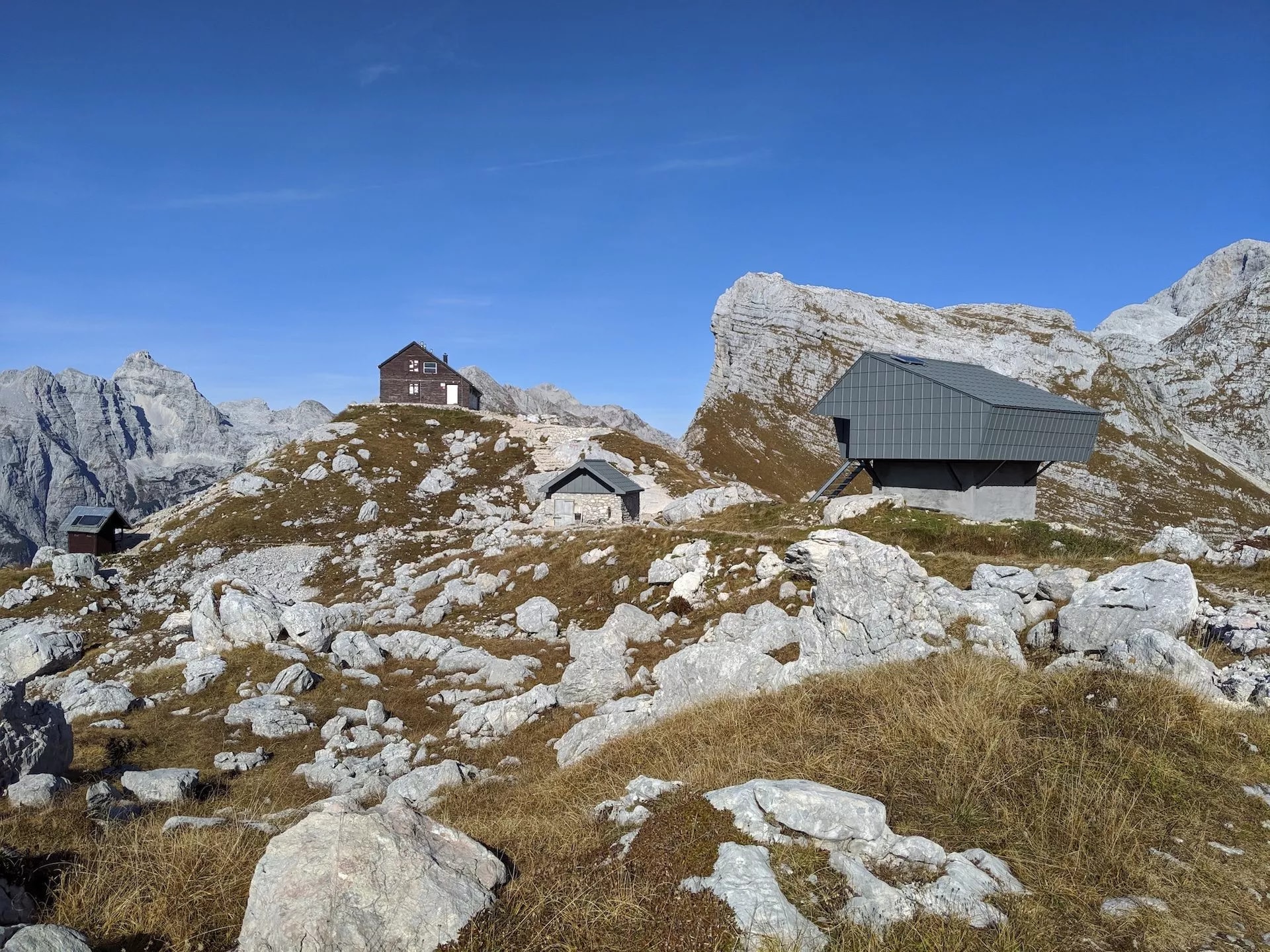 Prehodavci lodge and bivouac buildings on rocky alpine terrain under clear blue sky