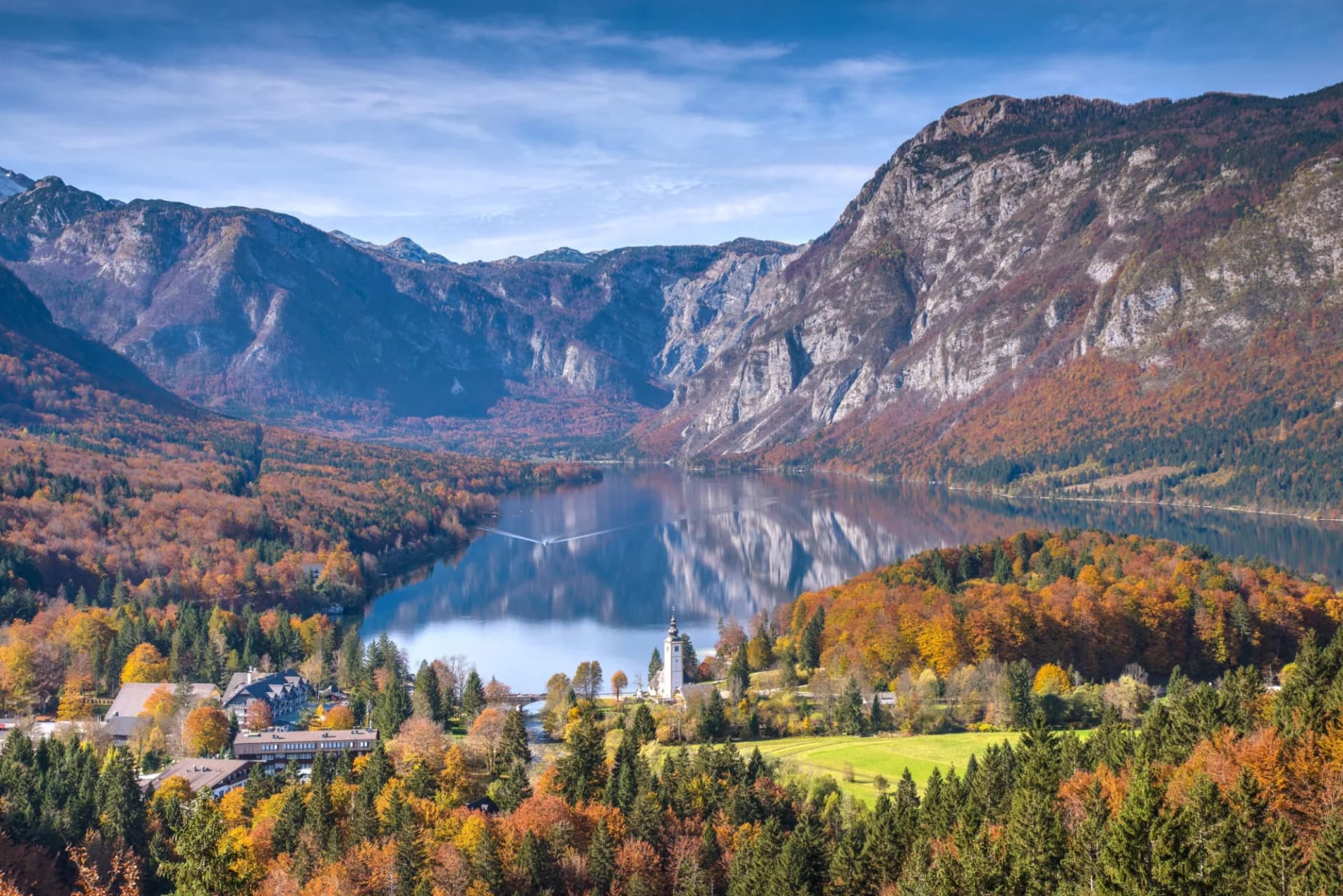 Lake Bohinj with autumn foliage, mountains, and St. John the Baptist Church in Slovenia.