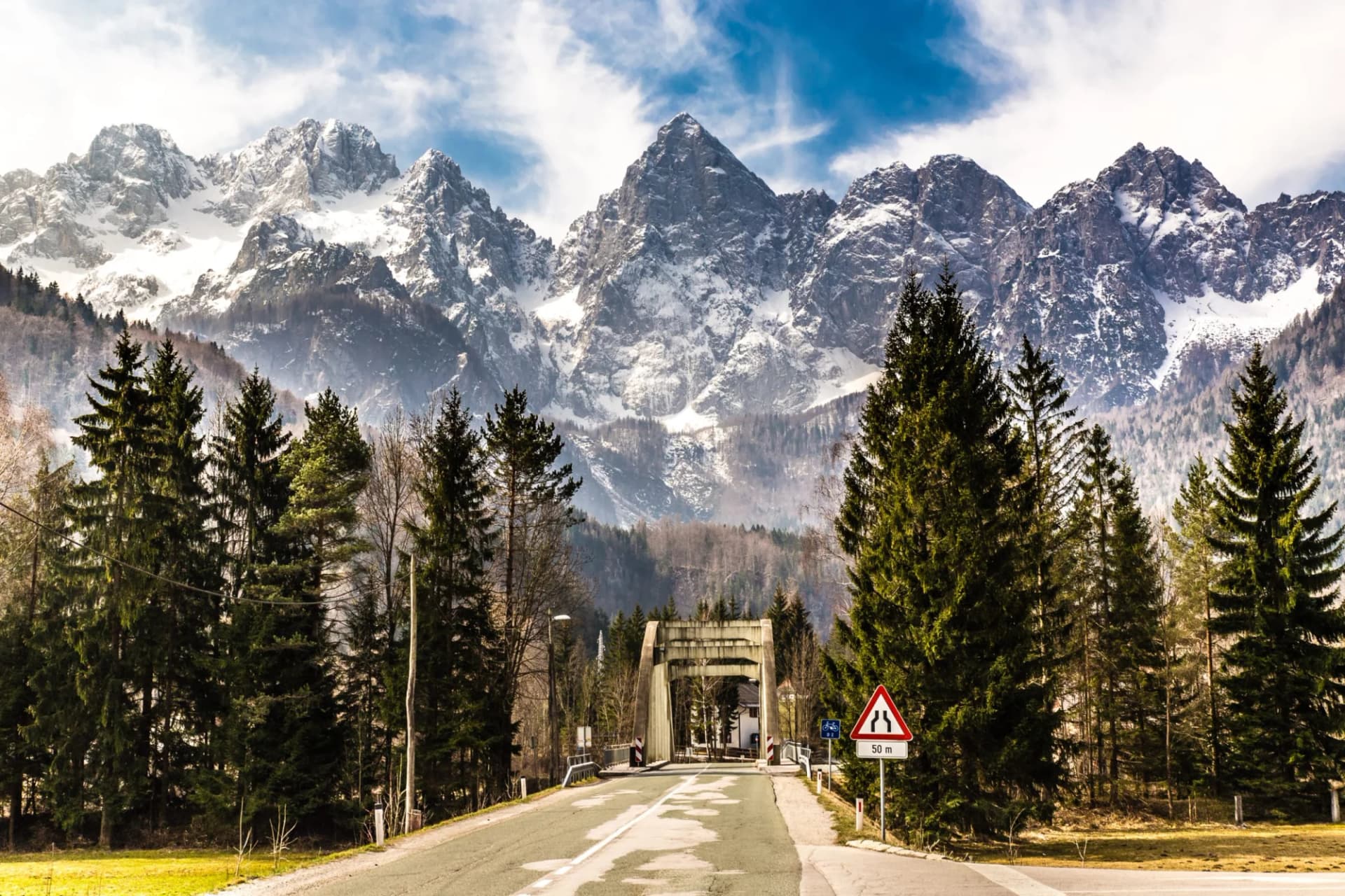 Road leading to a concrete bridge with snow-capped Spik Mountain in the background.