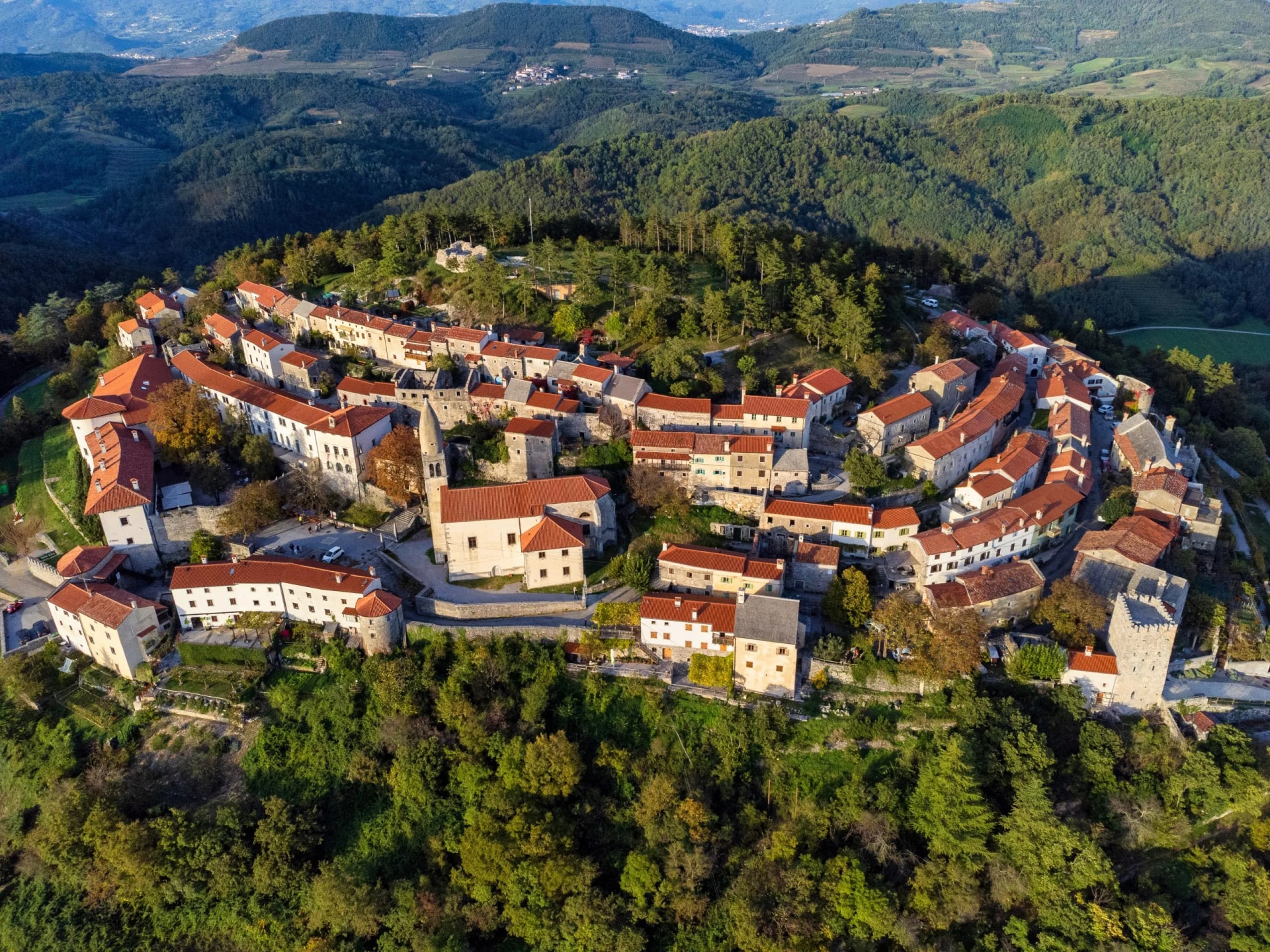 Hilltop historic town with red-tiled roofs surrounded by lush green forested hills in Stanjel.