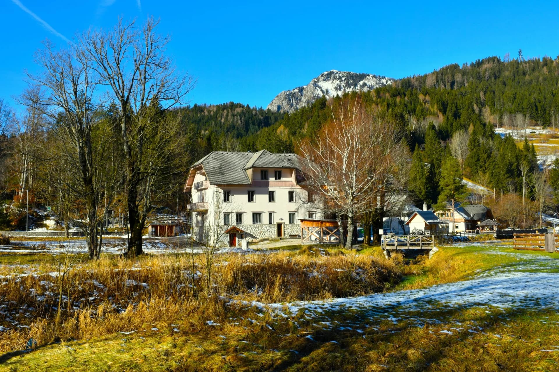 Building in Zgornje Jezersko village with snow-dusted mountains and forest backdrop