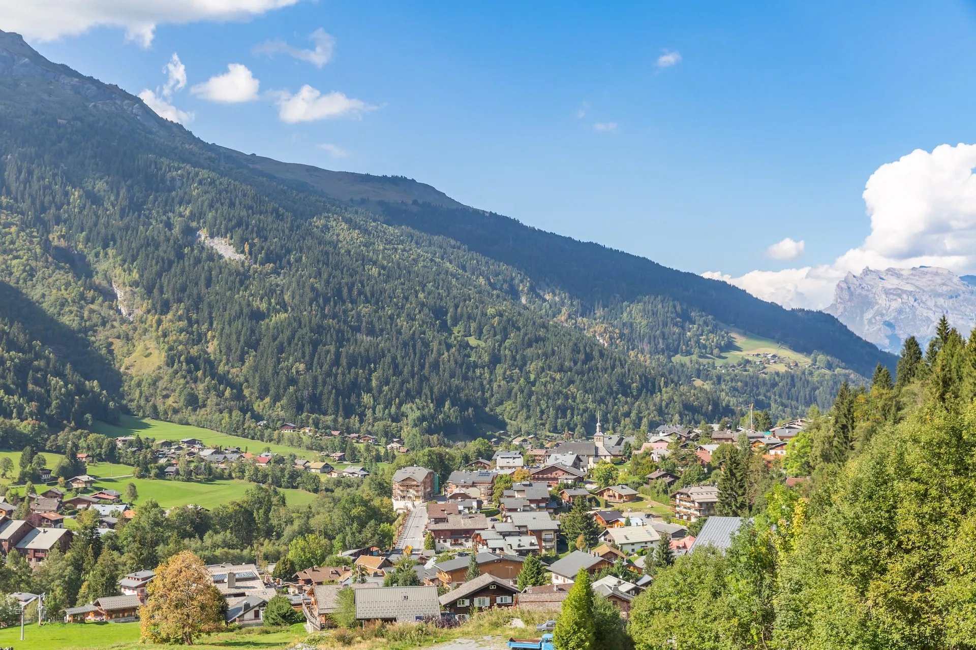 Alpine village of Les Contamines-Montjoie nestled in green valley below forested mountains under blue sky.