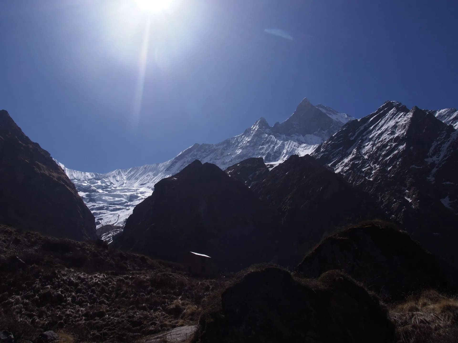 Trekking towards snow-capped Annapurna Base Camp mountains under bright sun in Nepal.