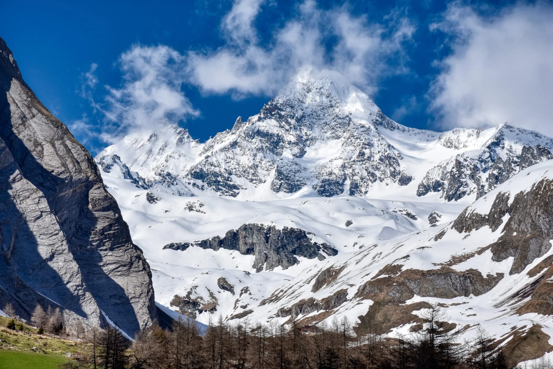 Snow-covered Grossglockner mountain peak under blue sky with clouds, view from valley floor.