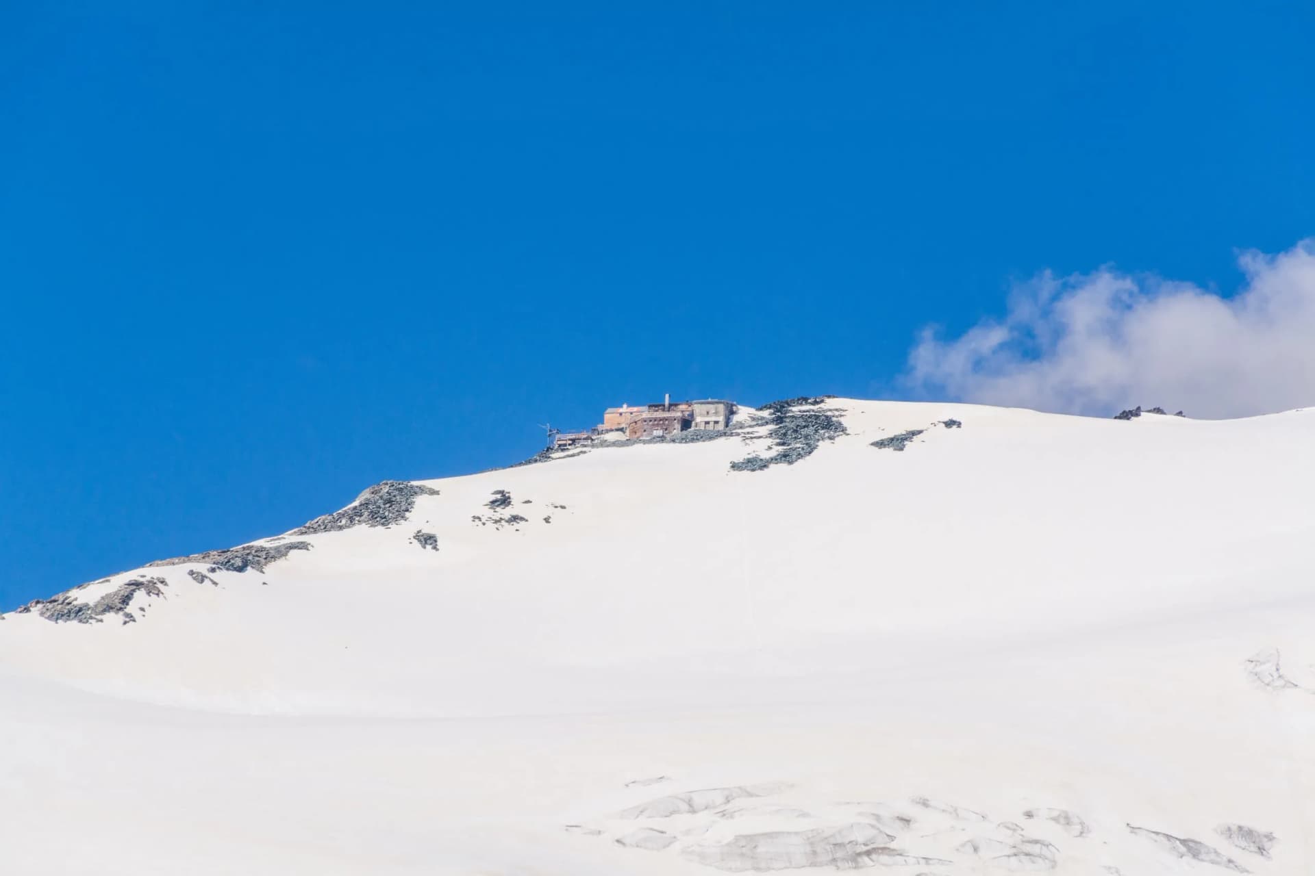 Erzherzog Johann Hütte mountain hut atop a snow-covered alpine peak under a bright blue sky.