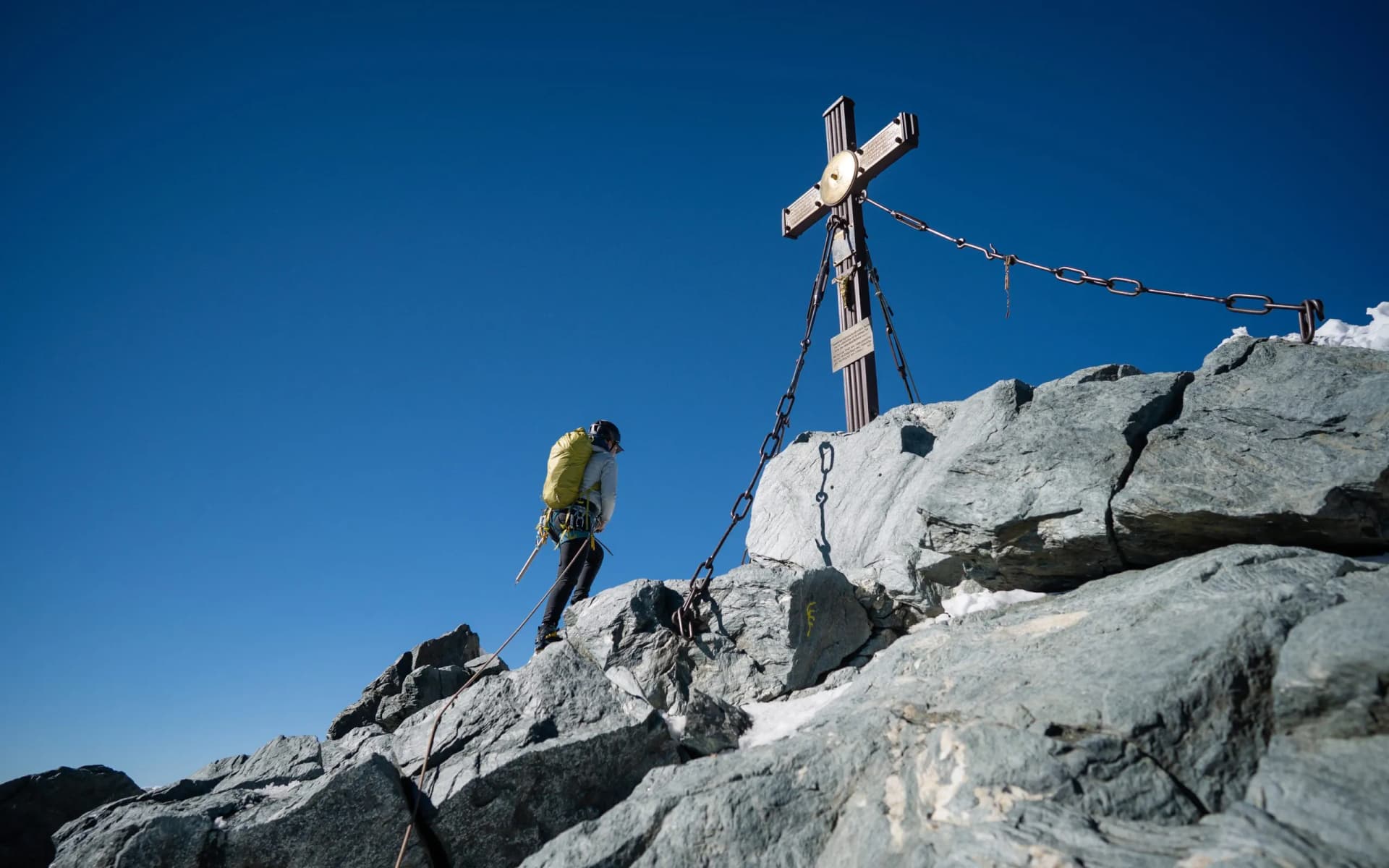 Hiker reaching summit cross on rocky Grossglockner peak under clear blue sky