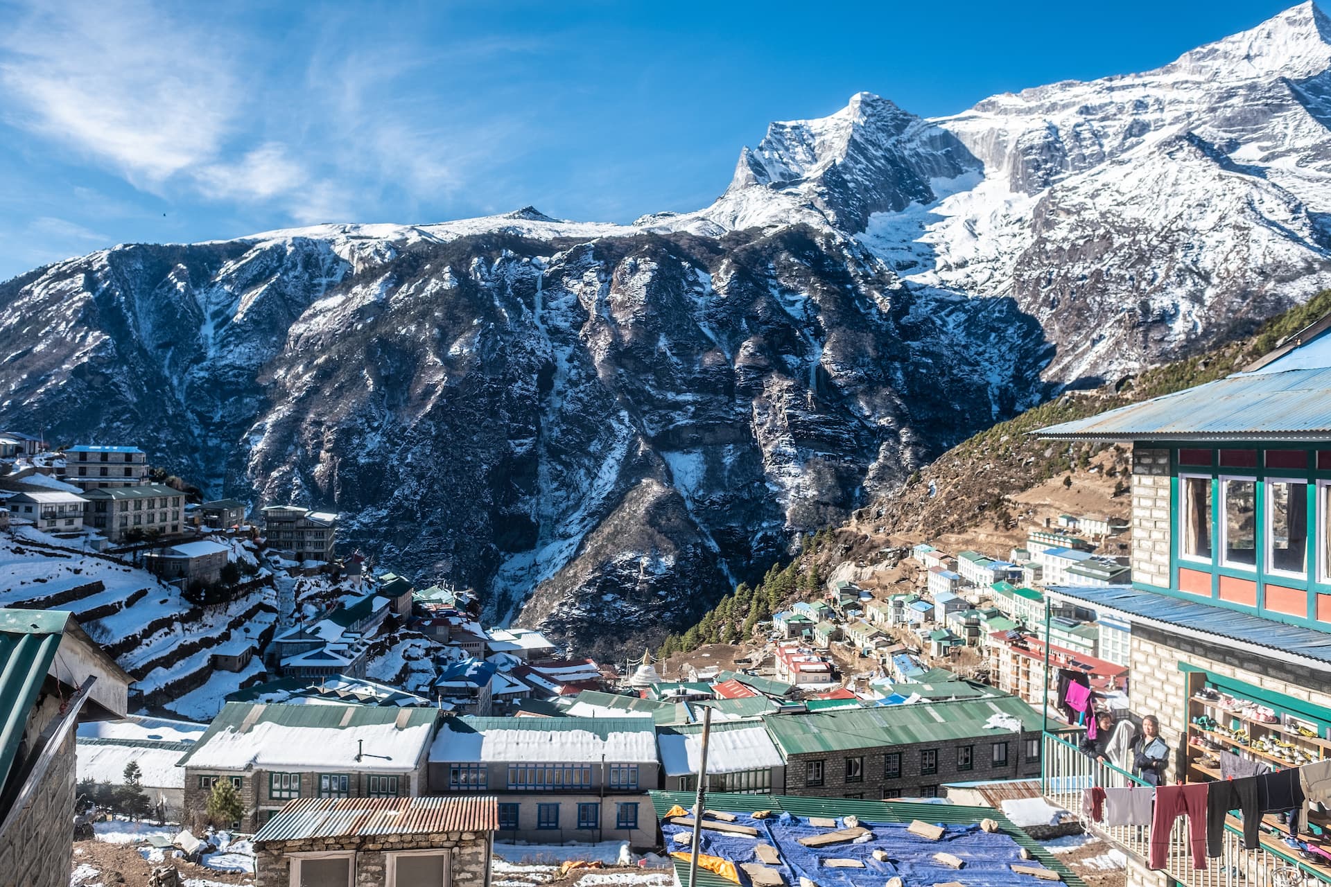 Top-down view of Namche Bazaar village nestled in snowy Himalayan mountains under a bright blue sky.