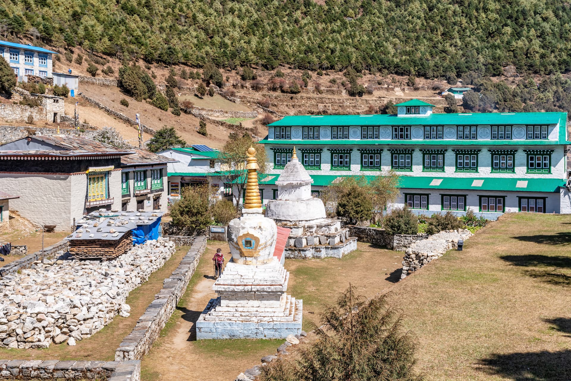 Buddhist stupas in Namche Bazaar with buildings and forested mountain slope background