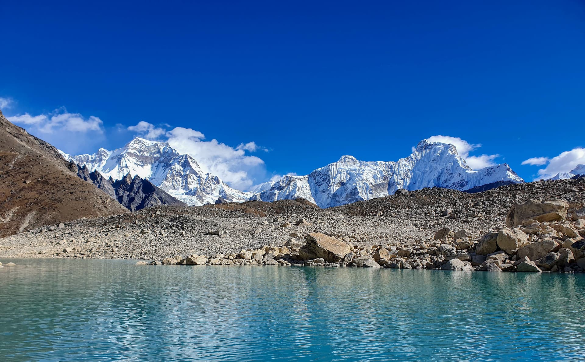 Turquoise alpine lake reflecting snow-capped mountains under a bright blue sky.