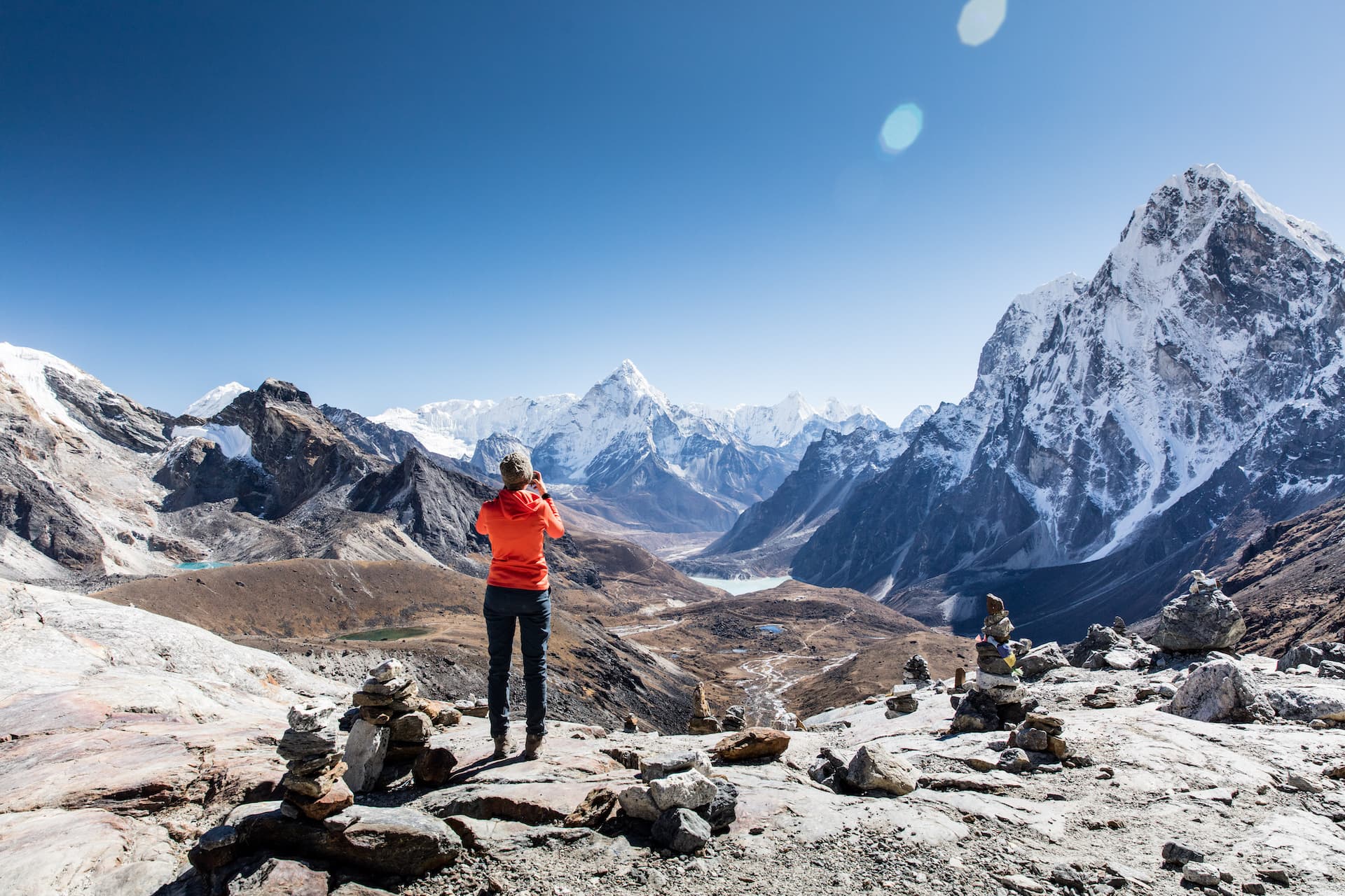 Hiker photographing snow-capped Himalayan mountains from Chola Pass viewpoint with cairns