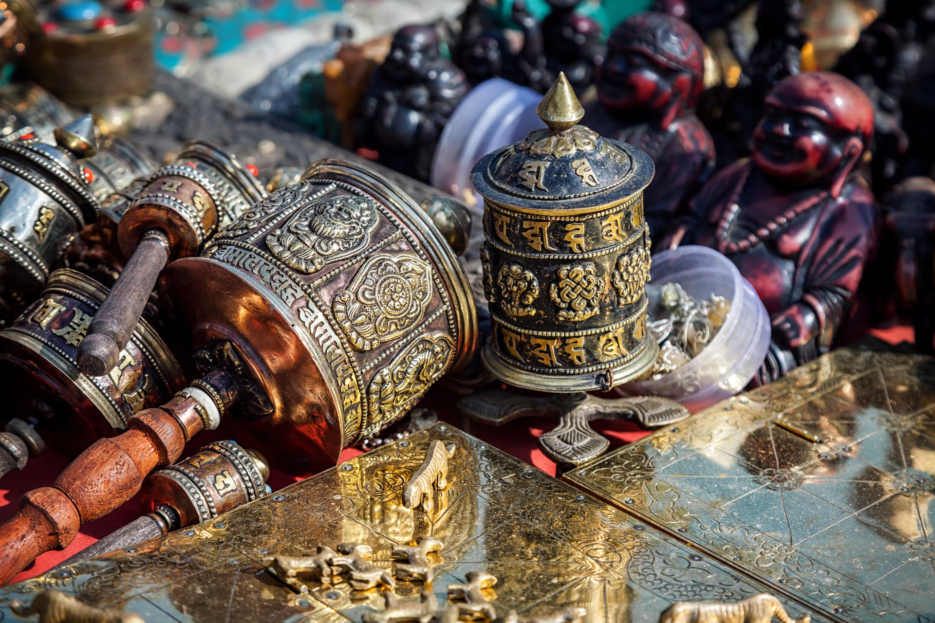 Ornate metal prayer wheels and small brass animal figures displayed outdoors in Kathmandu.