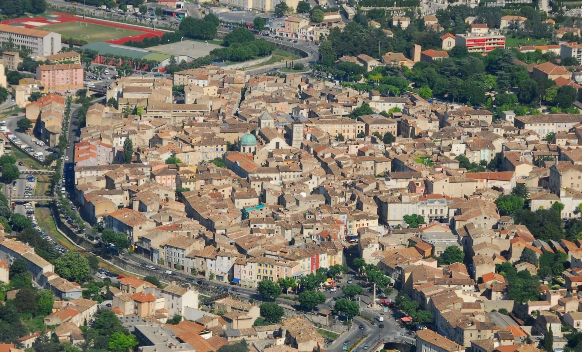 Aerial view of Apt town in Provence, showing dense terracotta roofs and a green dome.