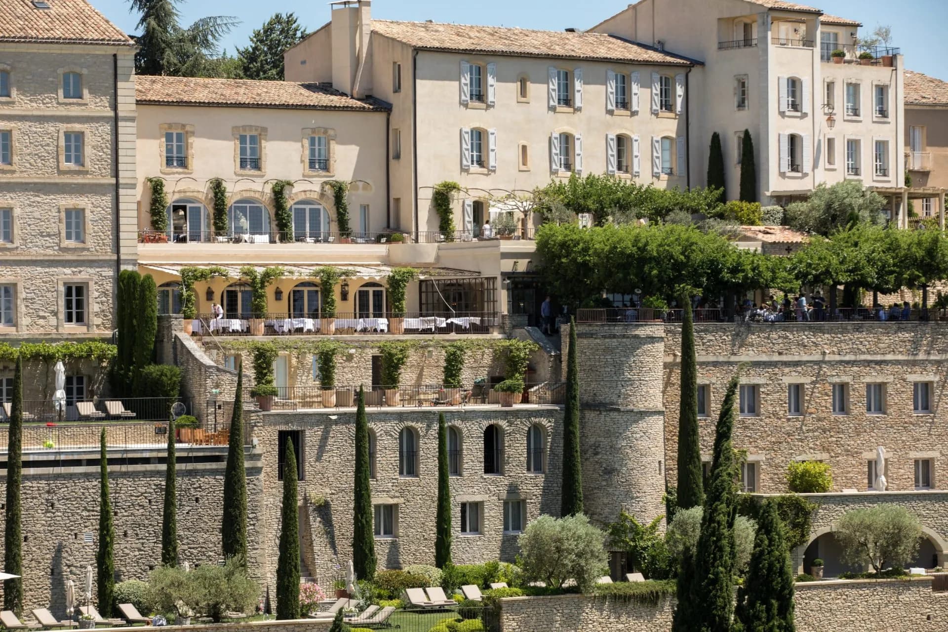 Stone hotel buildings with terraces and cypress trees, Gordes, France.