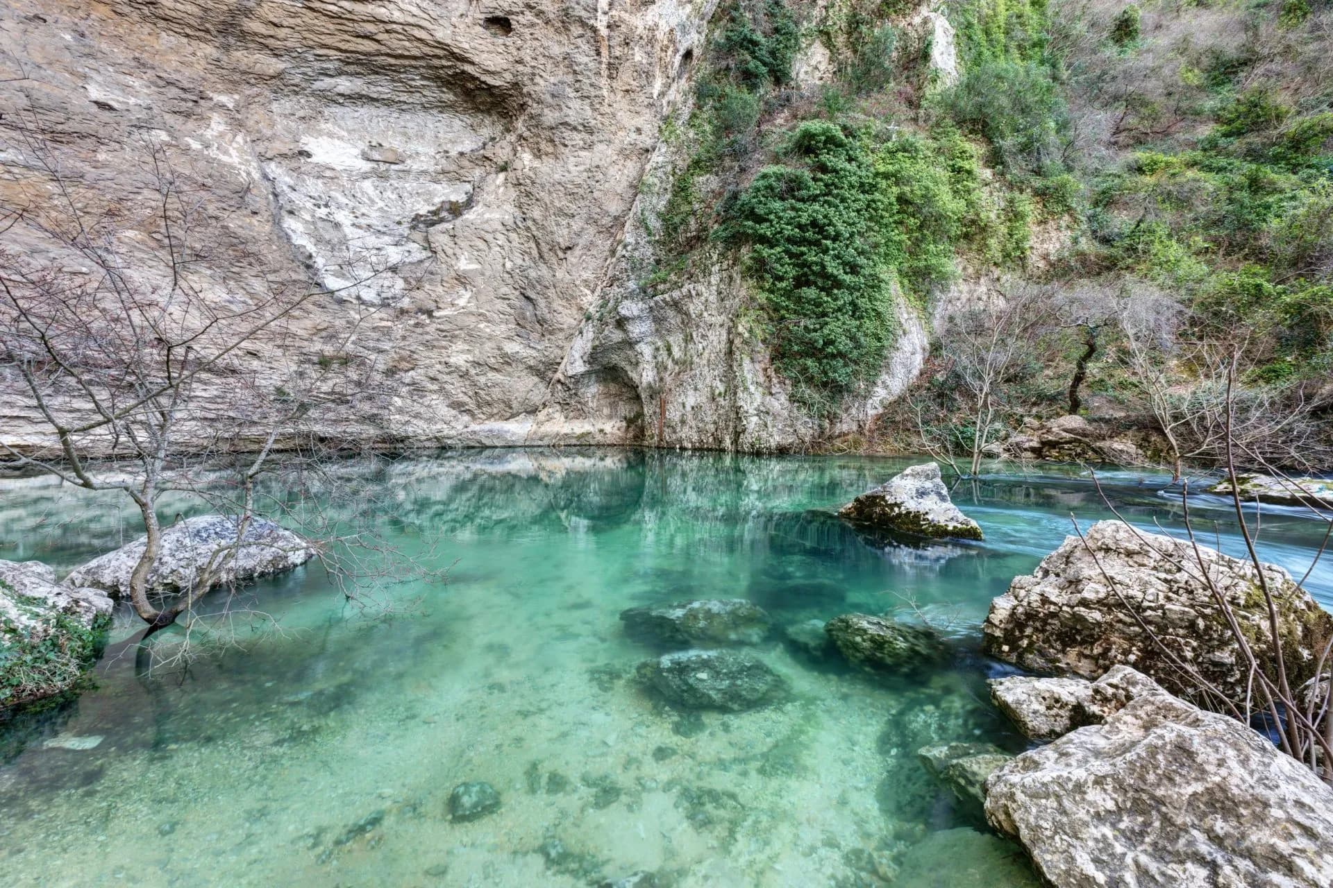Turquoise spring water pool at the base of a steep, rocky cliff in Fontaine-de-Vaucluse.