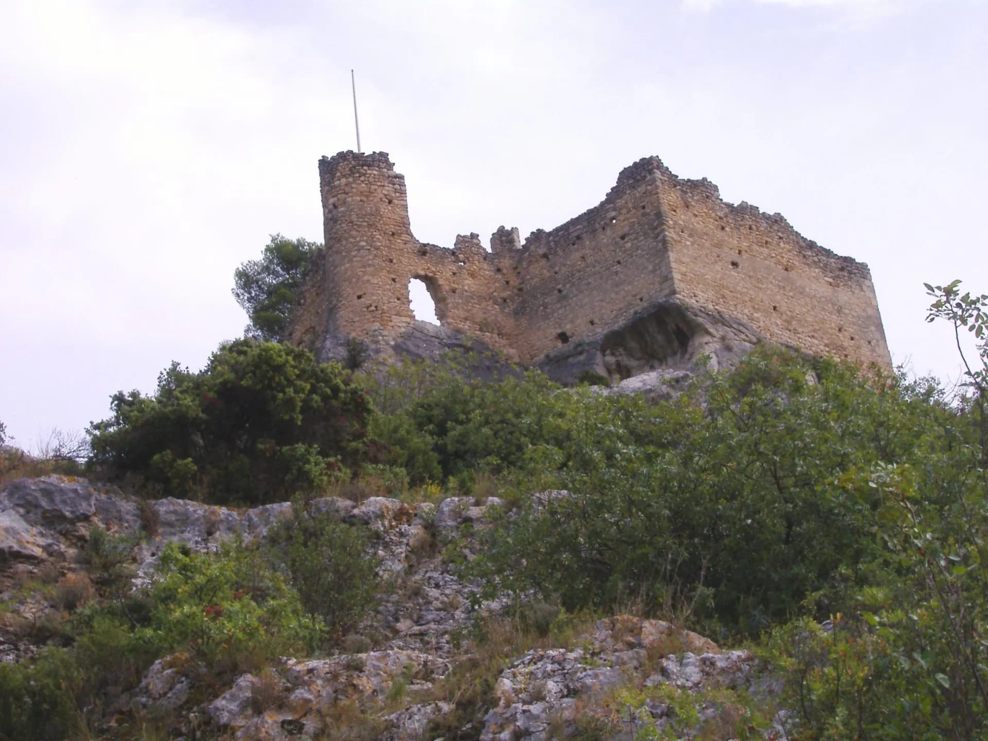 Stone castle ruins atop a rocky, scrub-covered hill under a bright sky in Fontaine de Vaucluse.
