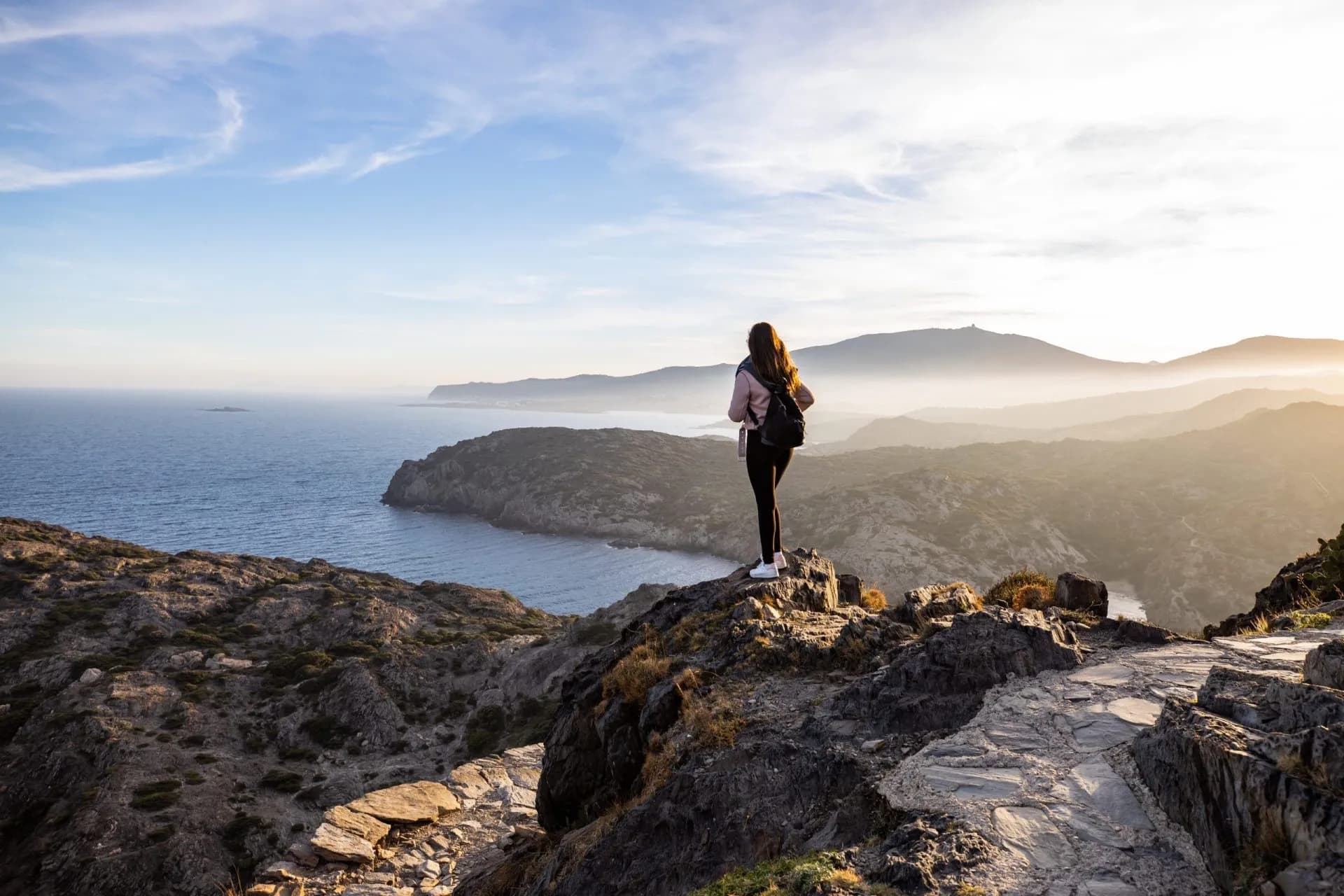 Hiker overlooking Cap de Creus rugged coastline and hazy mountains at sunset