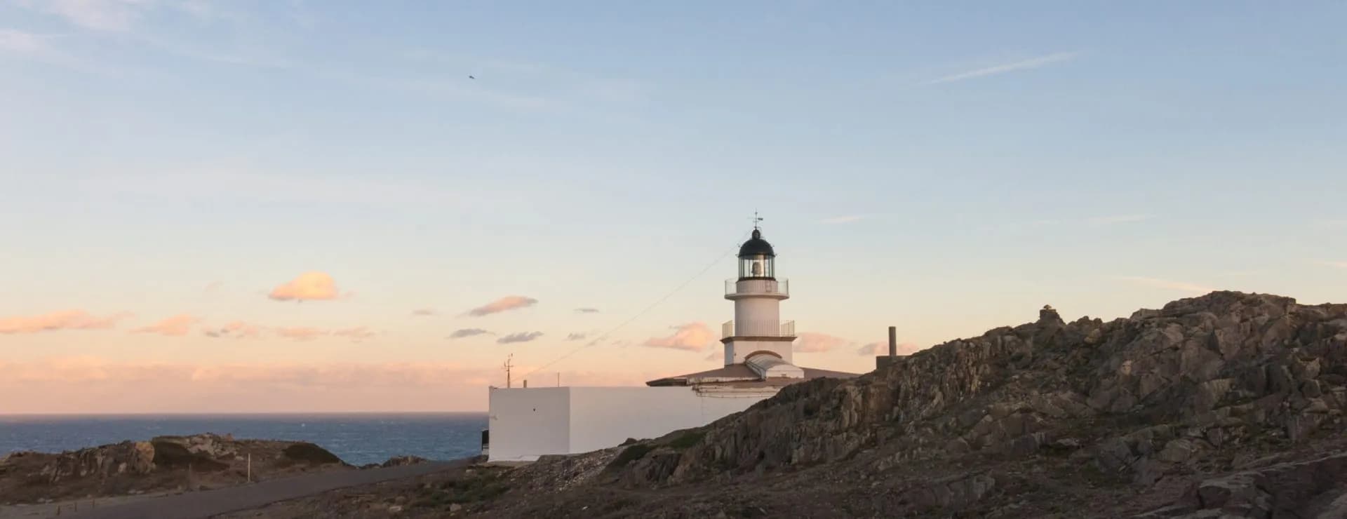 Cap de Creus lighthouse on rocky coastline overlooking the sea at sunset