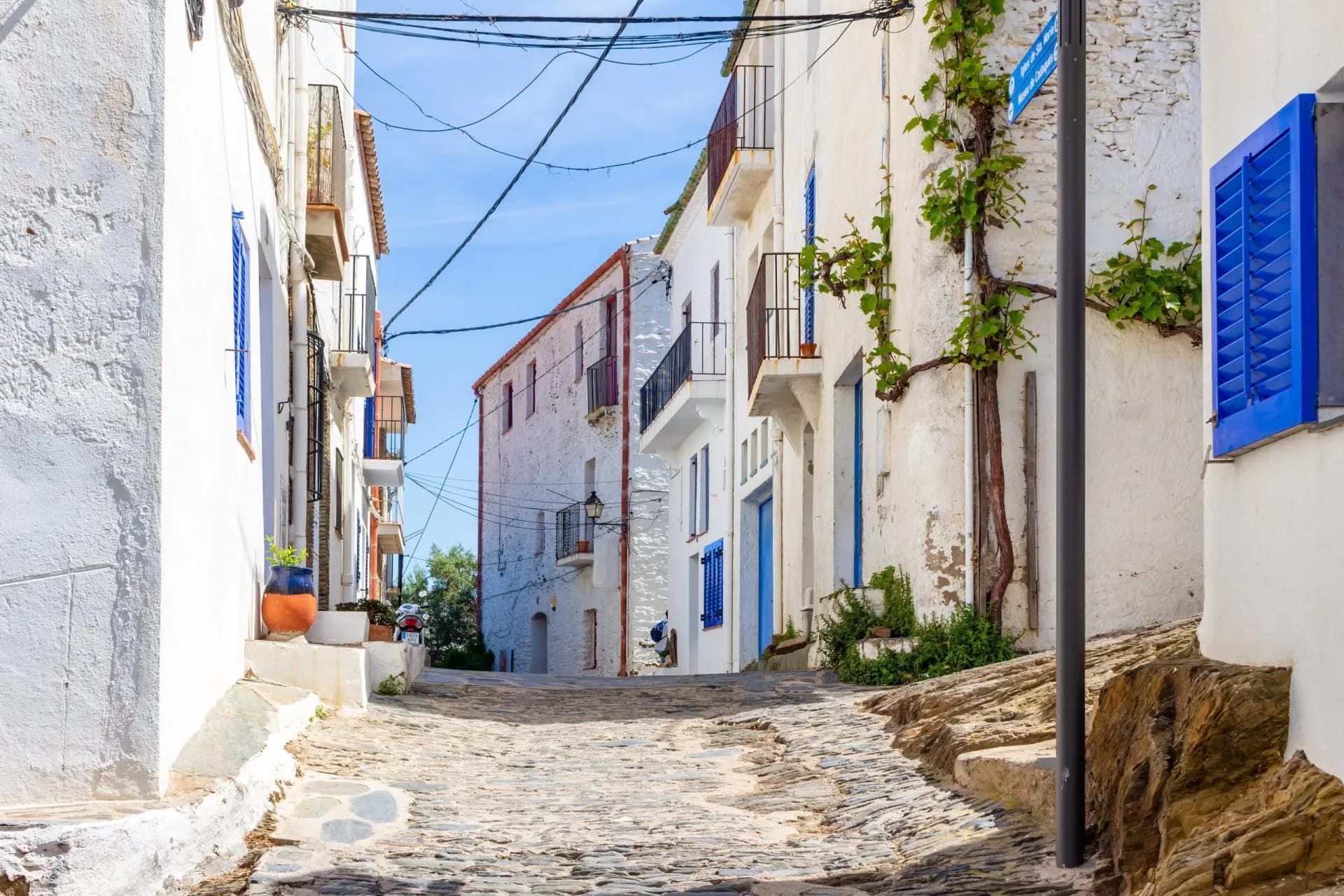 Cobblestone street sloping uphill between white buildings with blue shutters in Cadaques