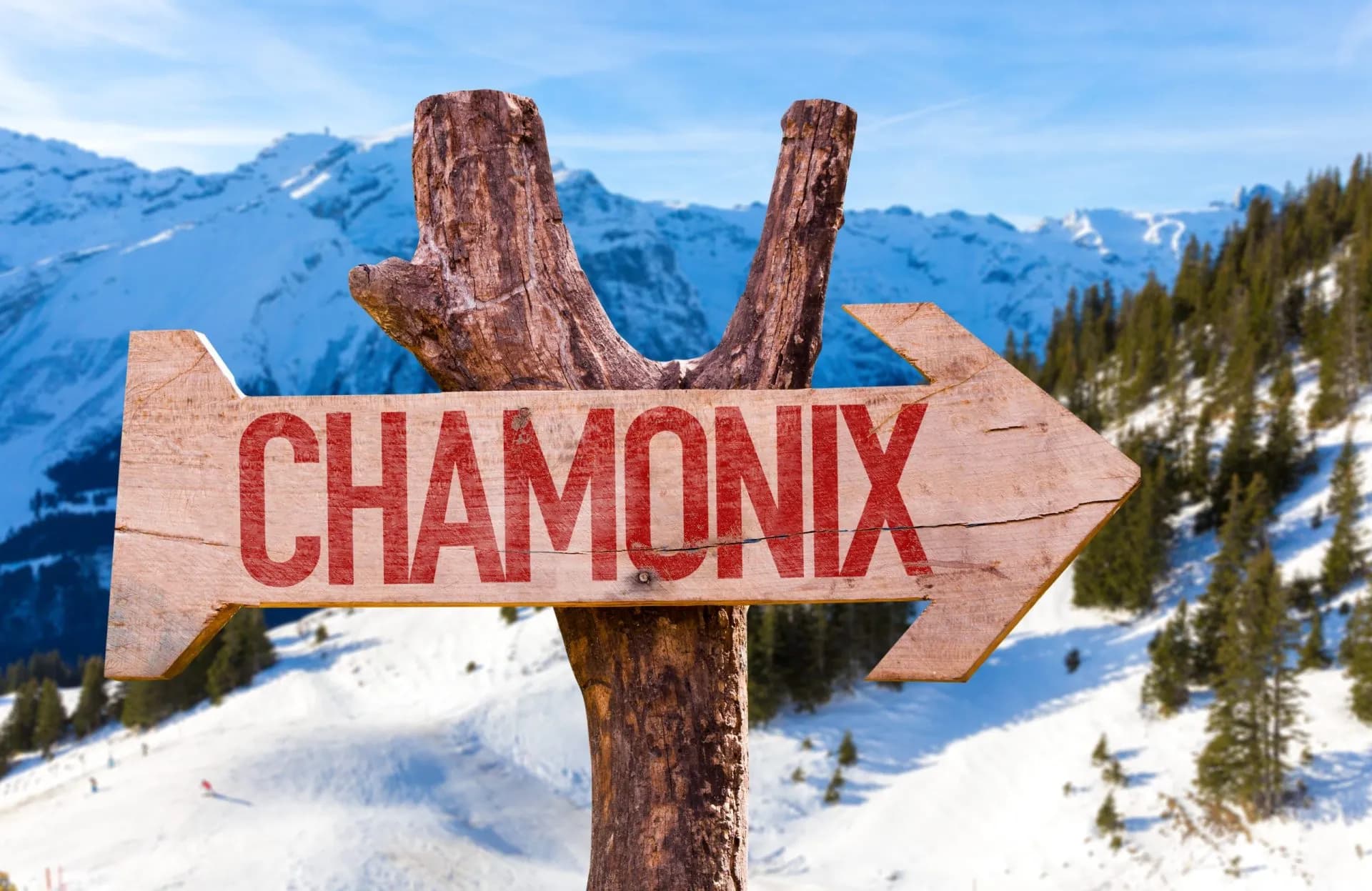 Wooden sign pointing to Chamonix with snowy mountains and ski slopes in background