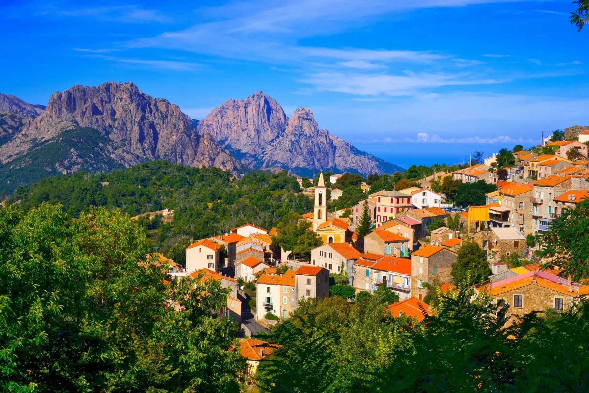 Hillside village with orange roofs, church tower, and rugged mountains in Corsica.