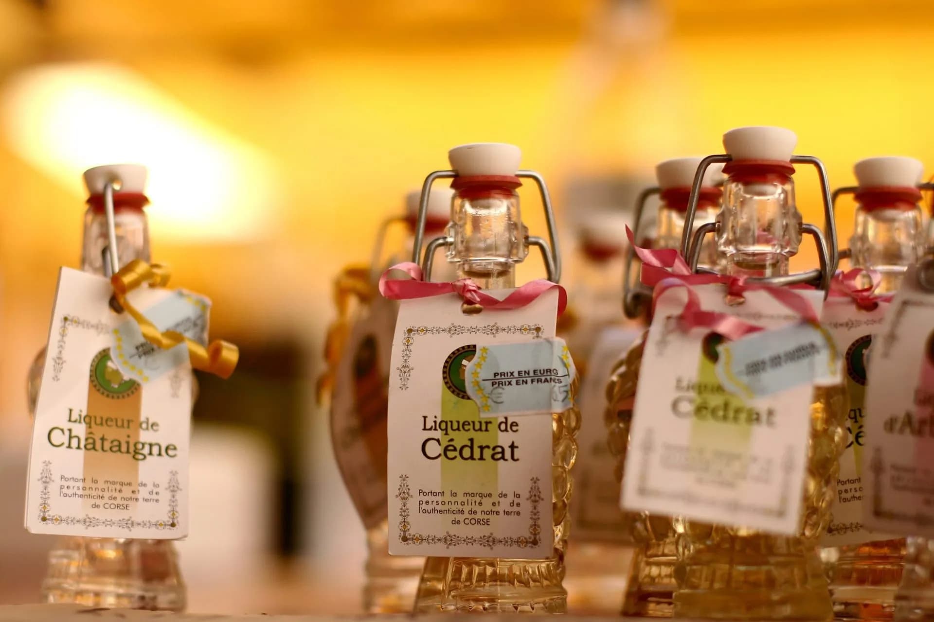 Corsican liqueur bottles with swing tops and tags, glowing in warm light