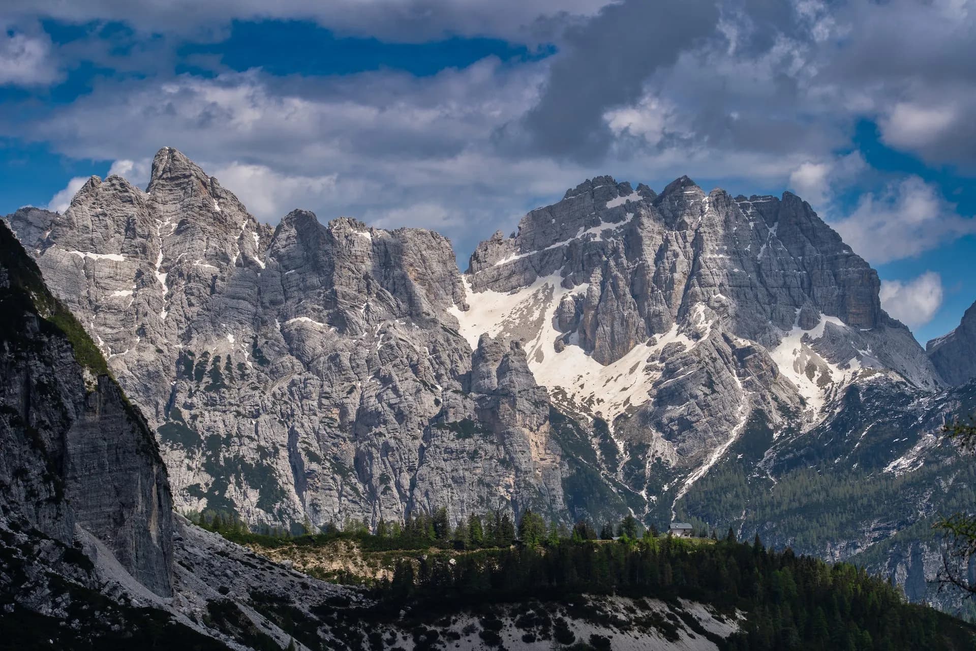 Rugged, rocky mountains with patches of snow above a dark green forest, Rifugio Carestiato on Col dei Pass.