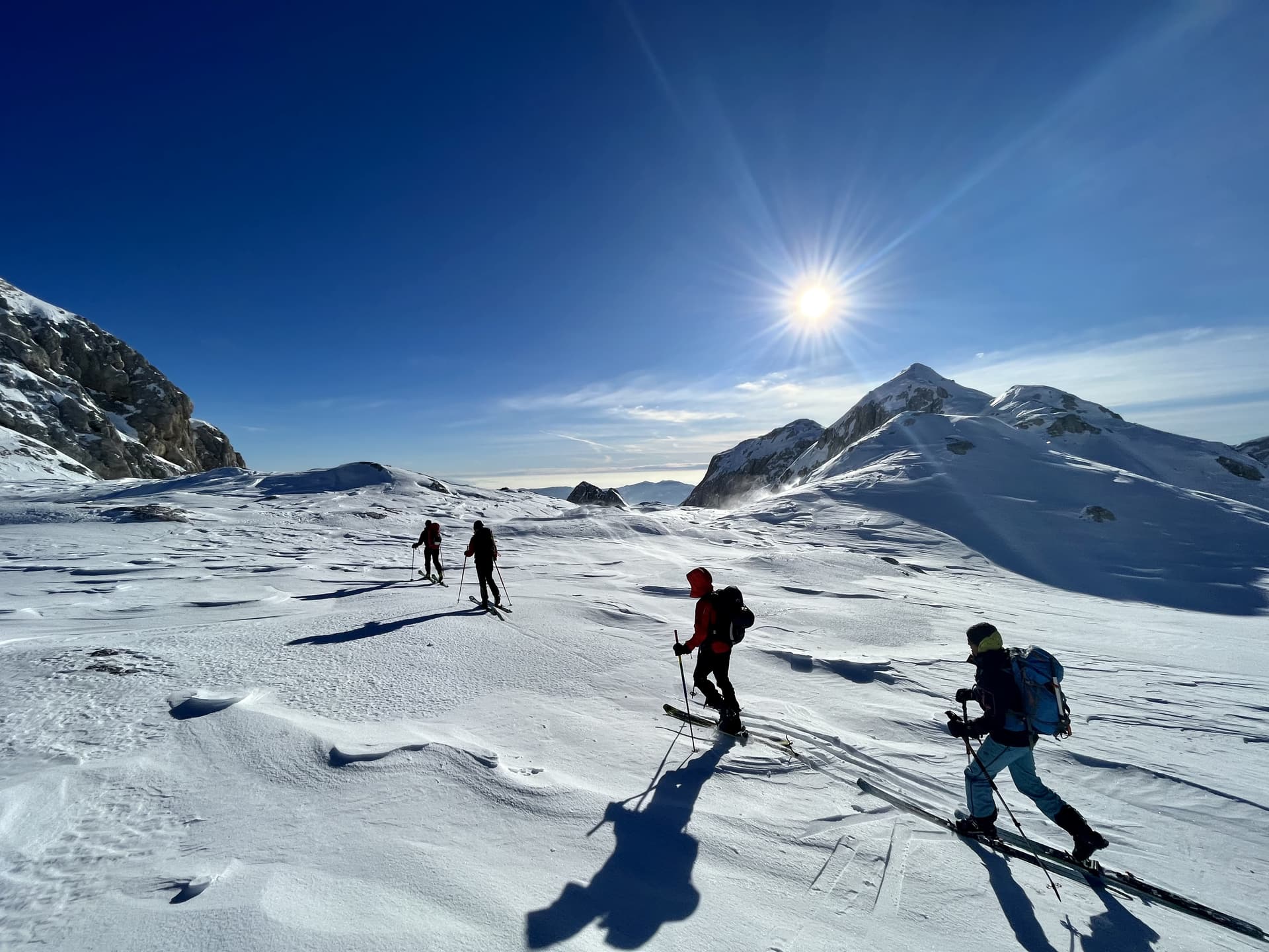 Ski touring on snow-covered alpine terrain under a bright sun near Kredarica.