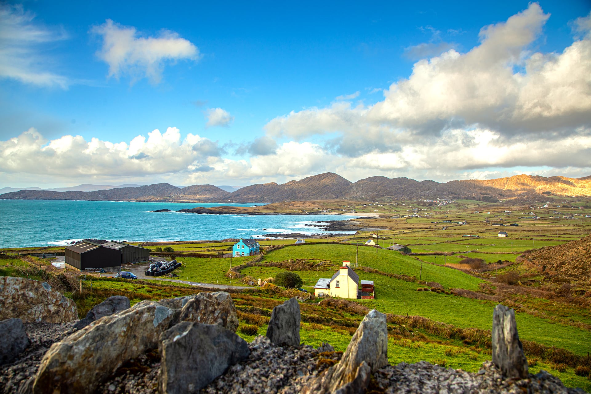 Staande stenen boven een baai van witte cottages en groene velden op het Beara-schiereiland