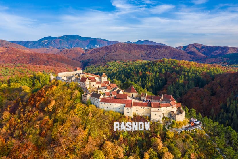 Medieval fortress Rasnov in Transylvania, Romania, on a hill surrounded by autumn foliage and mountains.